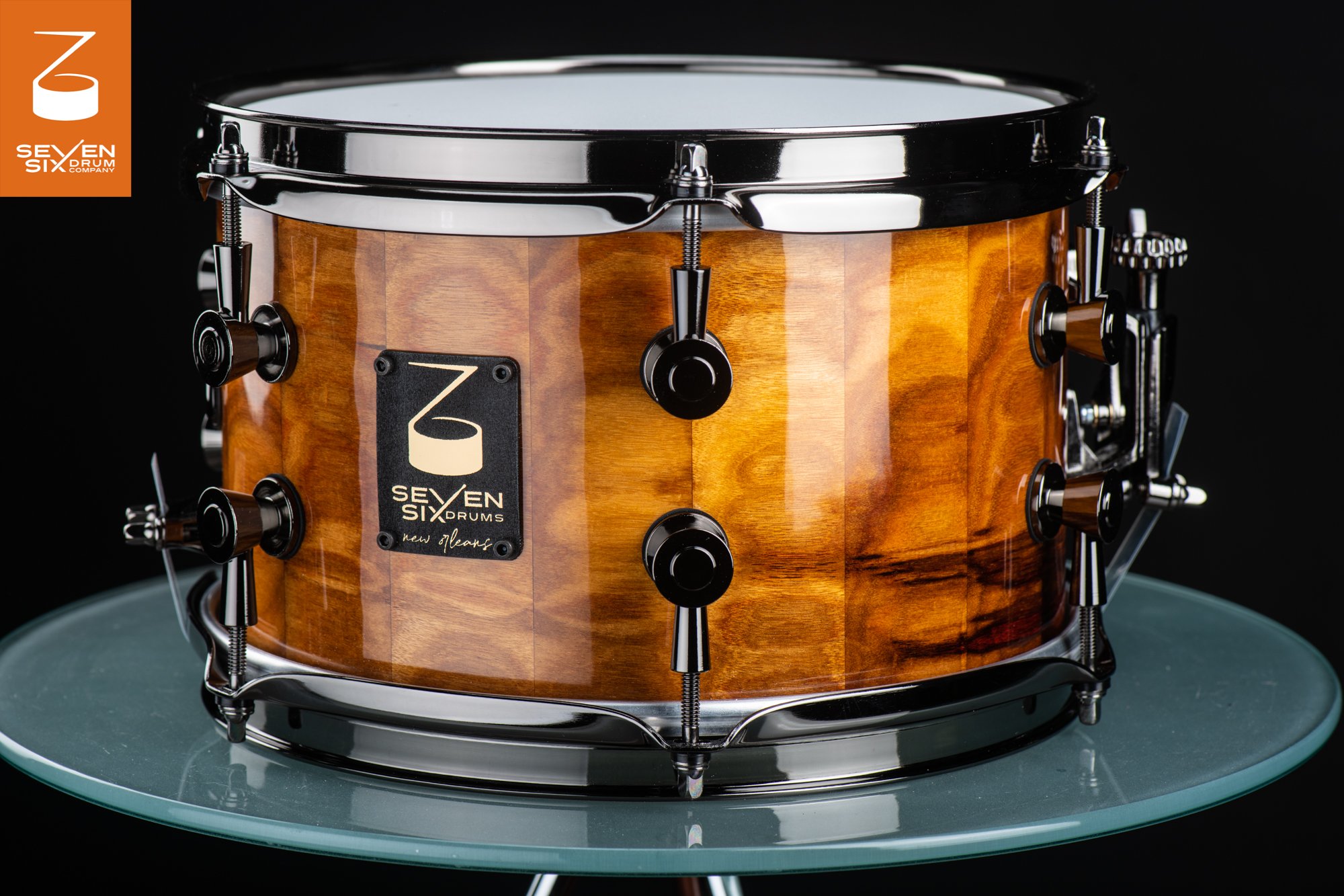 Handmade snare drum featuring a glossy golden wood stave shell with black nickel hoops and hardware.