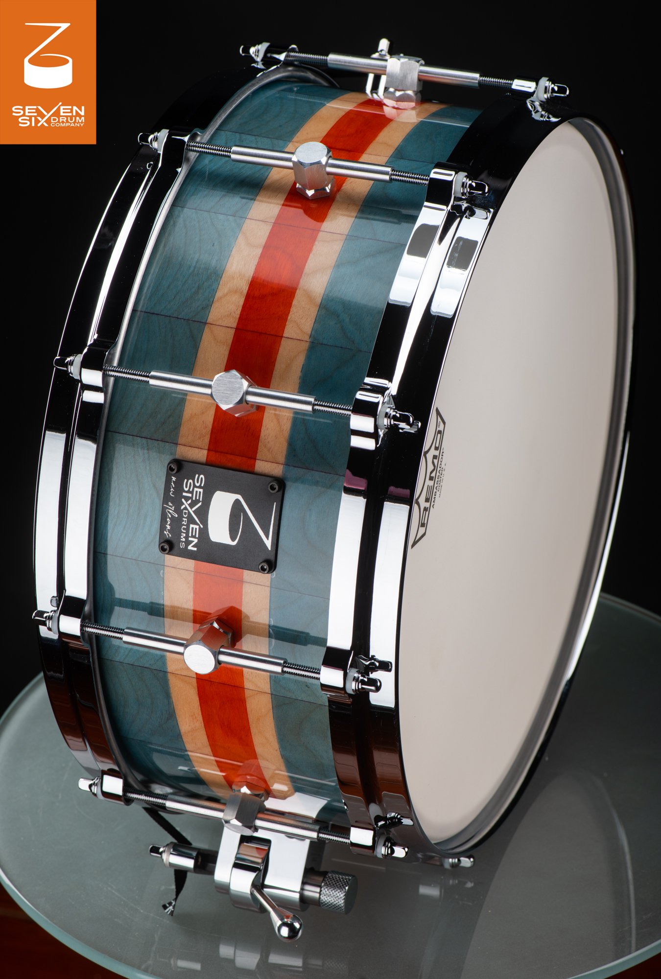 Custom snare drum with a glossy teal and red striped wood shell, chrome hoops, and single-point tube lugs.