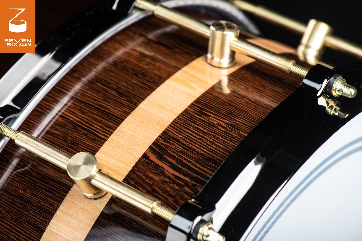 Glossy dark wood snare drum with a light wood center stripe, featuring brass tube lugs and a black metal hoop.