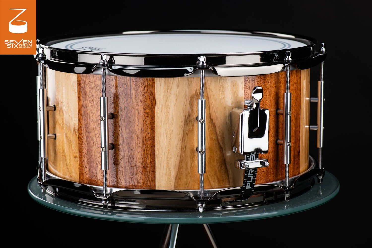 Handmade stave snare drum in gloss alternating light and dark wood with chrome tube lugs, hoops, and throw-off.