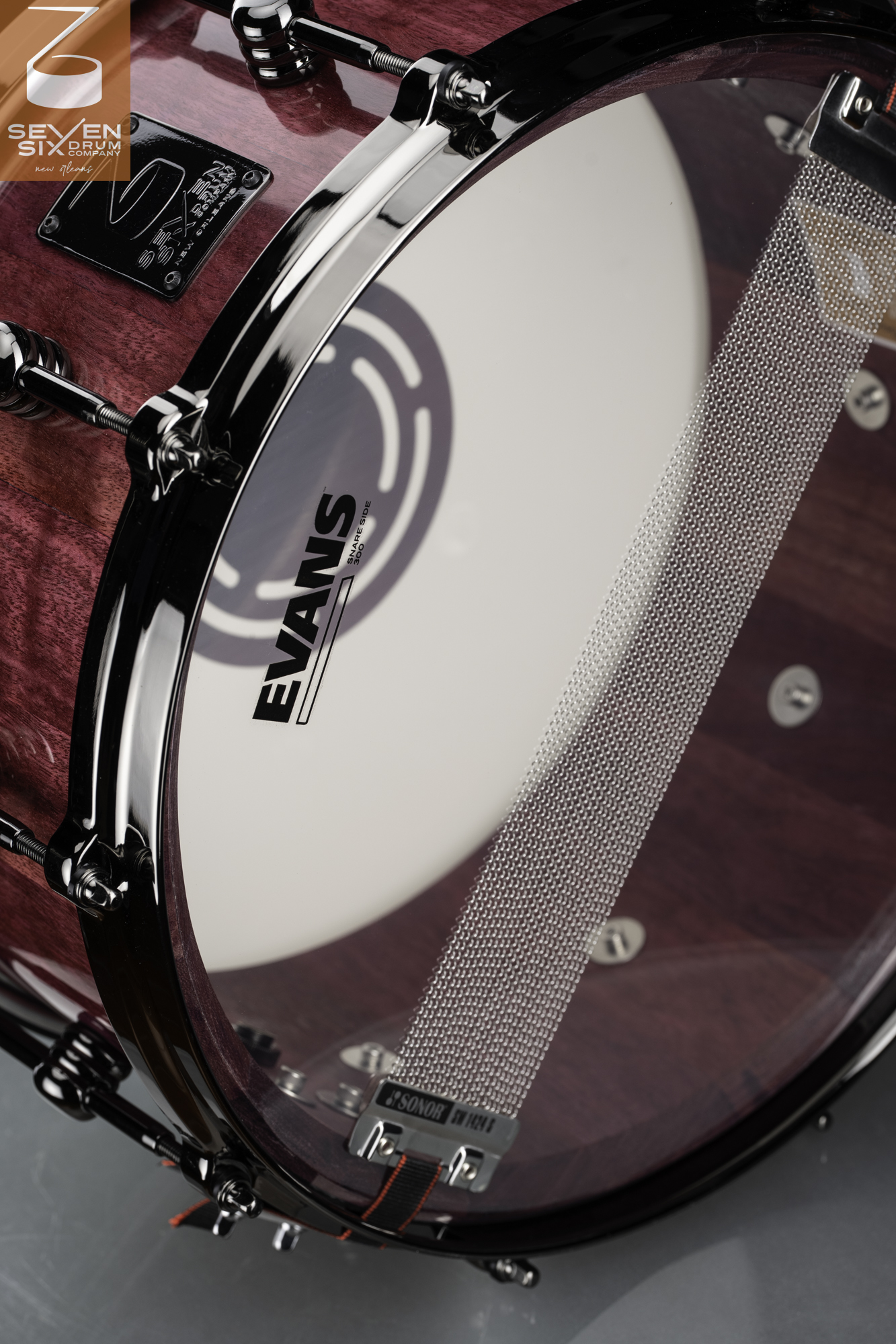 Handmade purple wood snare drum with a glossy finish, black nickel hoops, and Sonor snare wires over an Evans head.
