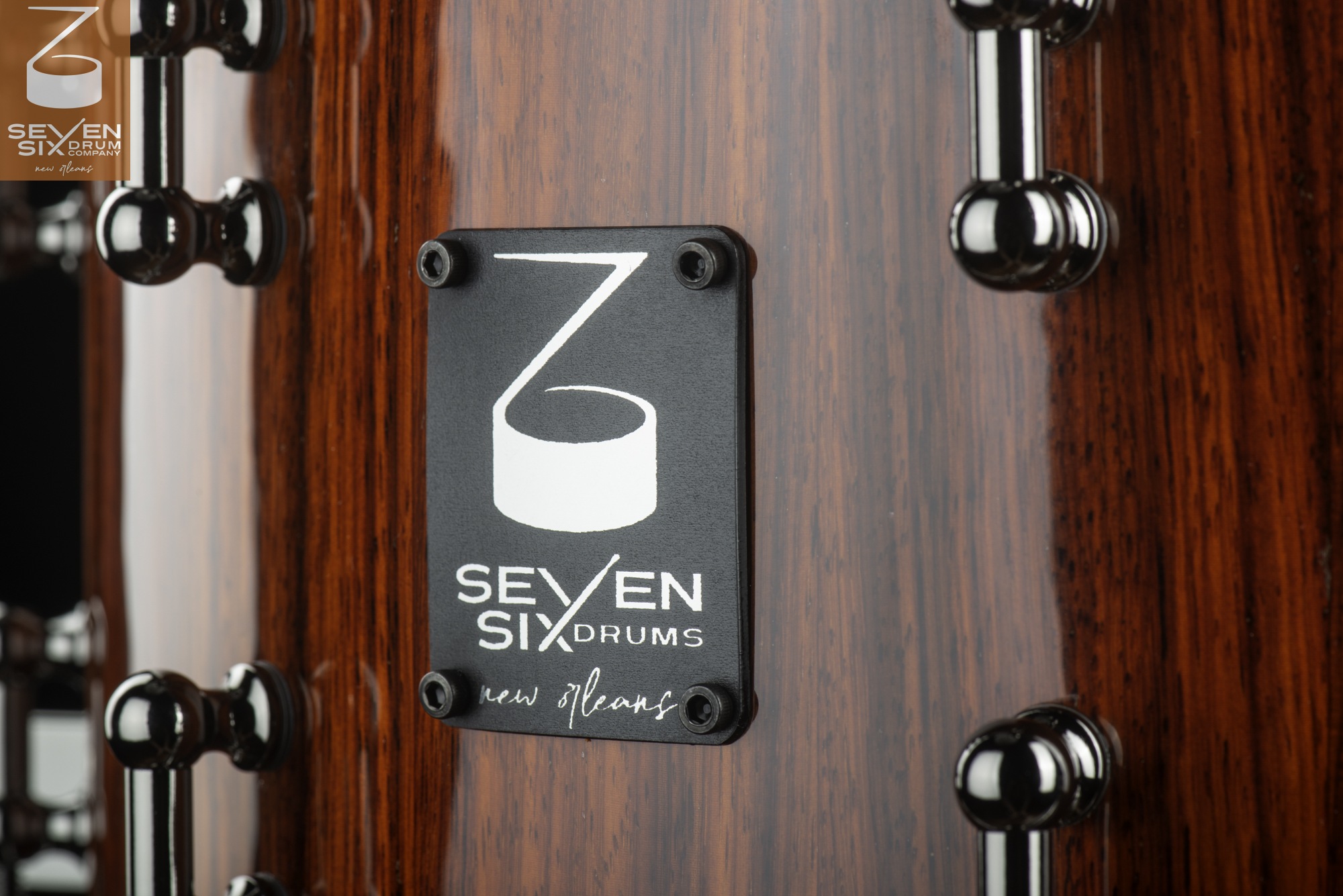 Close-up of a gloss red wood snare drum shell with a black Seven Six Drums badge and polished chrome tube lugs.