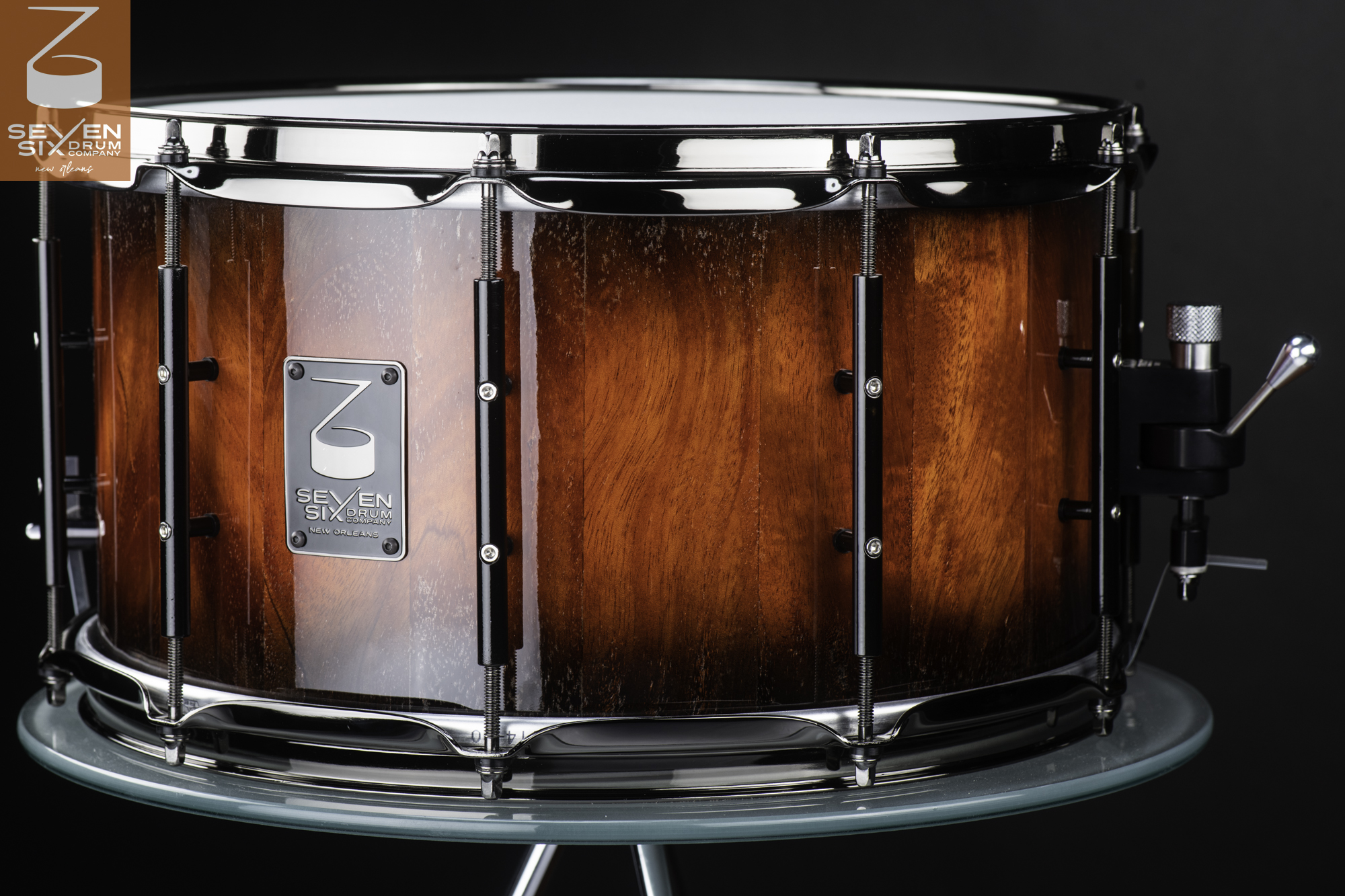 Glossy reddish-brown wood snare drum featuring chrome hoops, black tube lugs, and a side throw-off strainer.