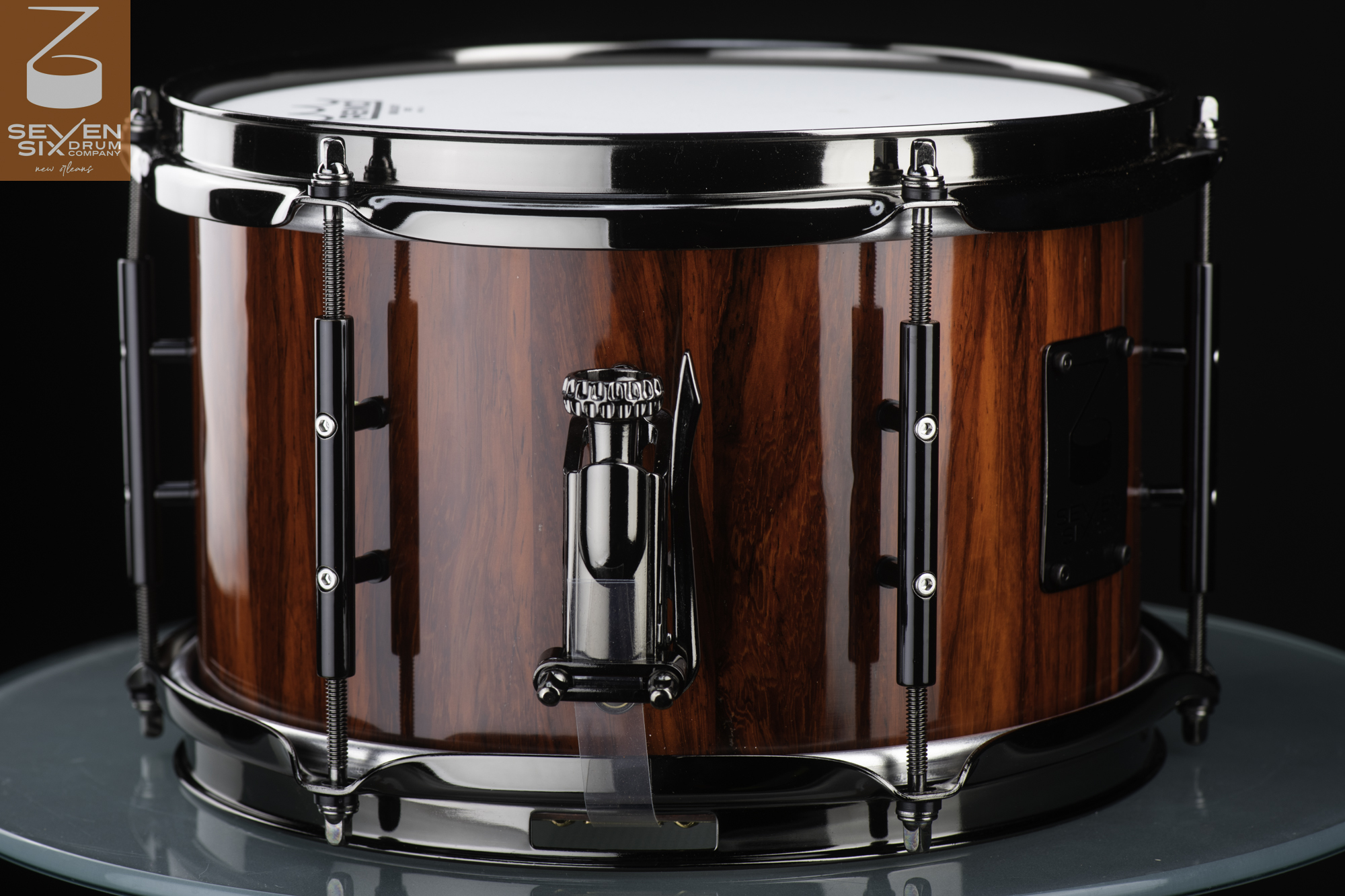 Handmade wood snare drum with a glossy reddish-brown finish, black nickel hardware, tube lugs, and throw-off.