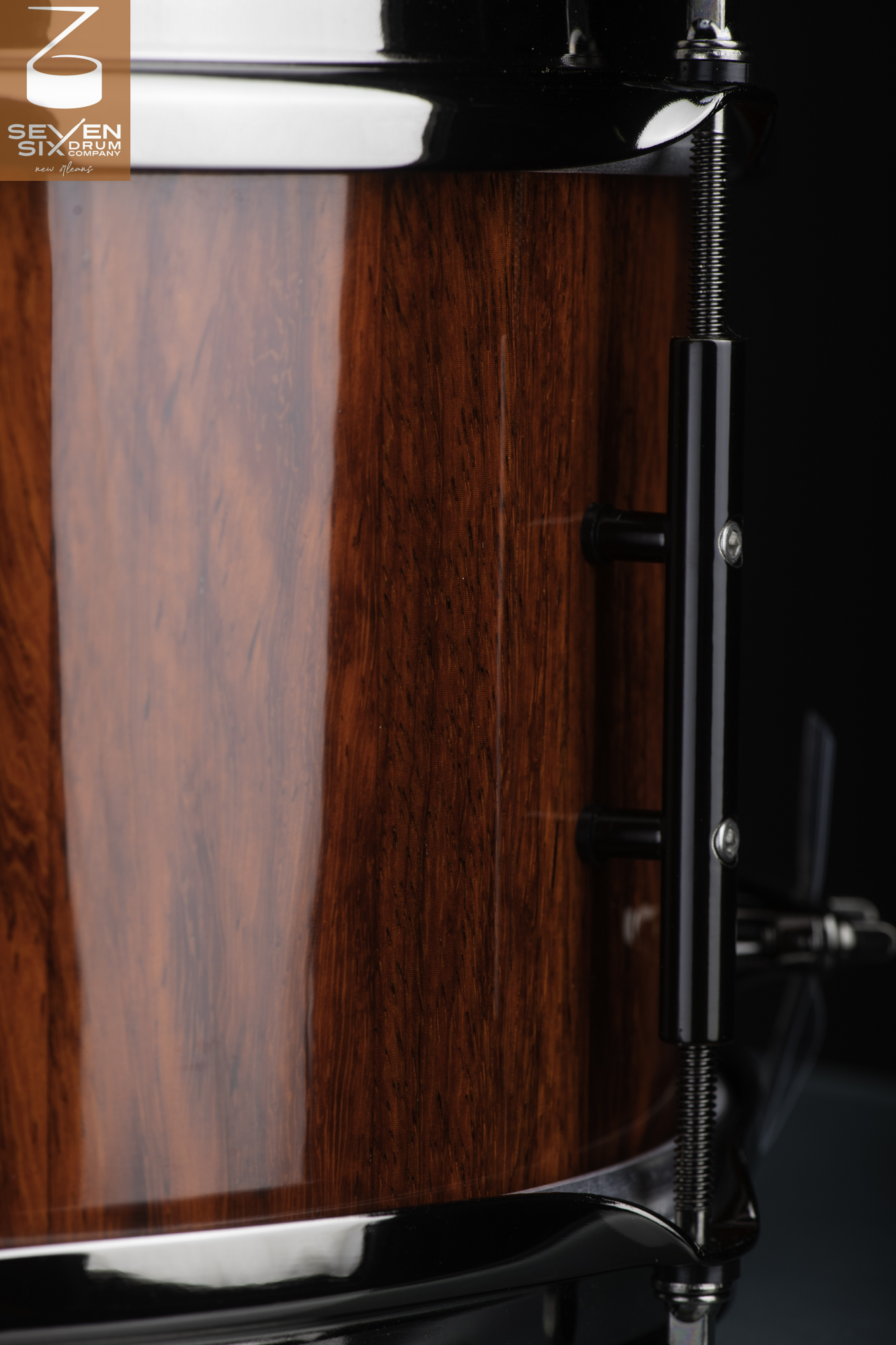 Handmade snare drum with a high-gloss reddish wood finish, black tube lug, and polished black hoops.