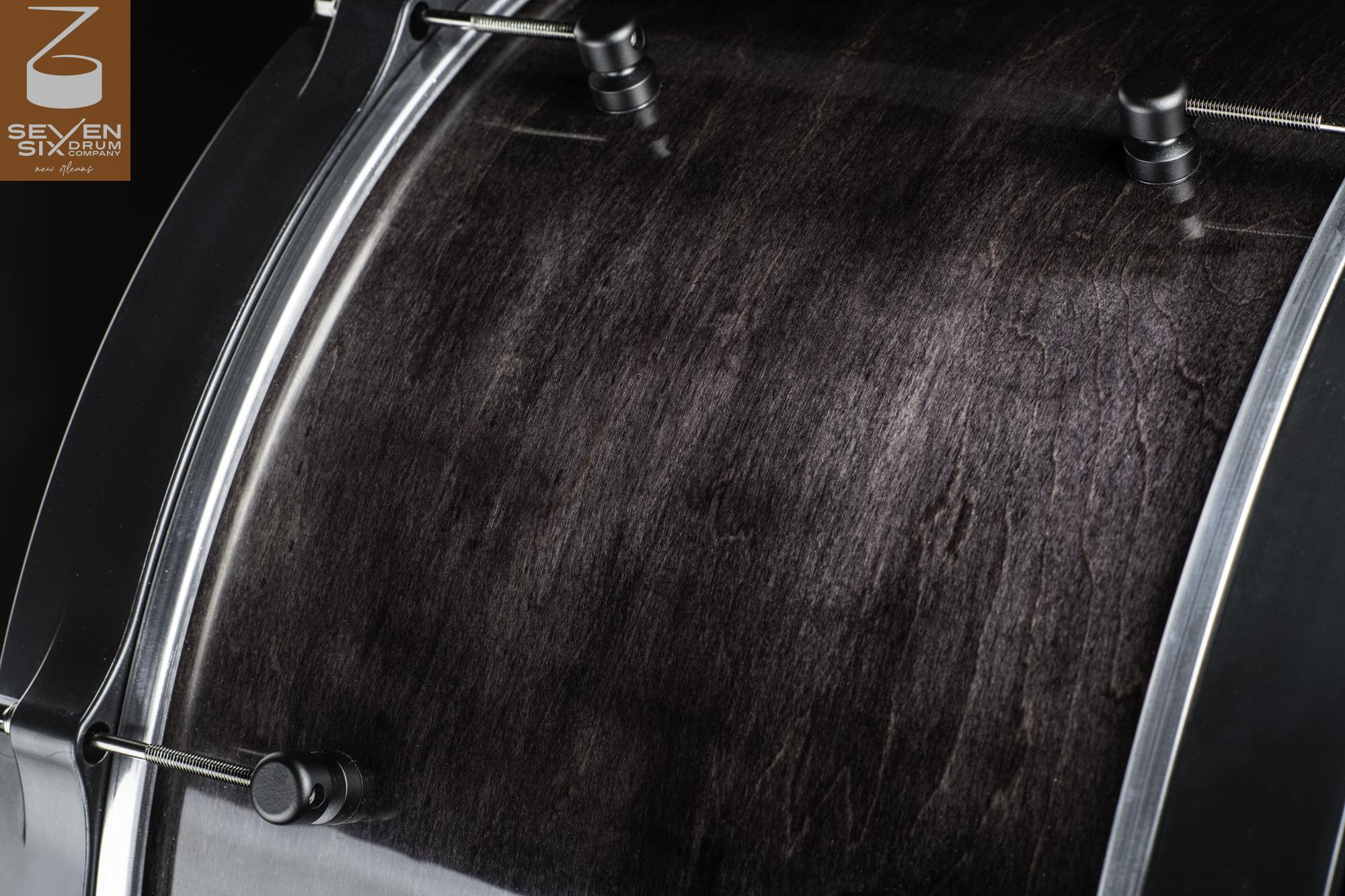 Handmade snare drum shell with a dark stained wood grain finish, round black lugs, and black metal hoops.