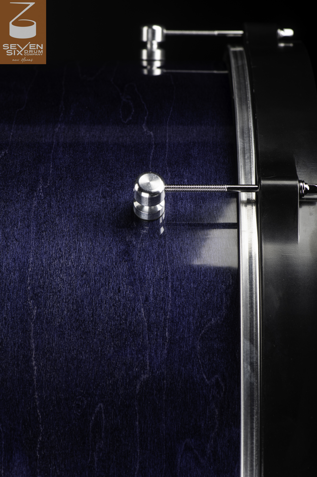 Close-up of a snare drum with a blue-stained wood finish, round brushed aluminum lugs, and a black hoop.