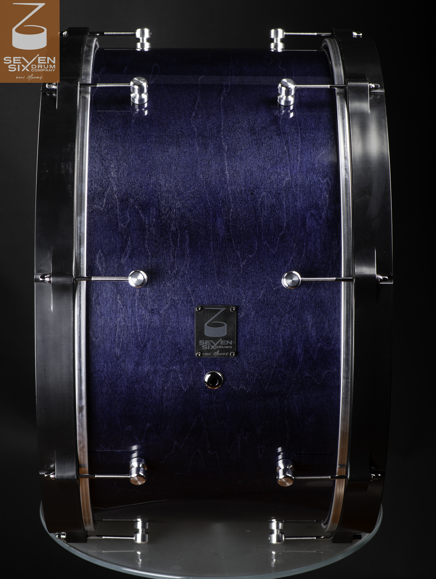 Handcrafted bass drum with a dark blue stained wood shell, wide black hoops, and chrome lugs.