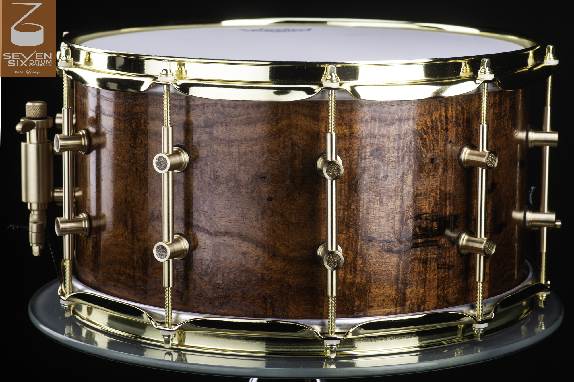 Handmade snare drum with a glossy figured wood shell, polished brass tube lugs, and matching brass hoops.