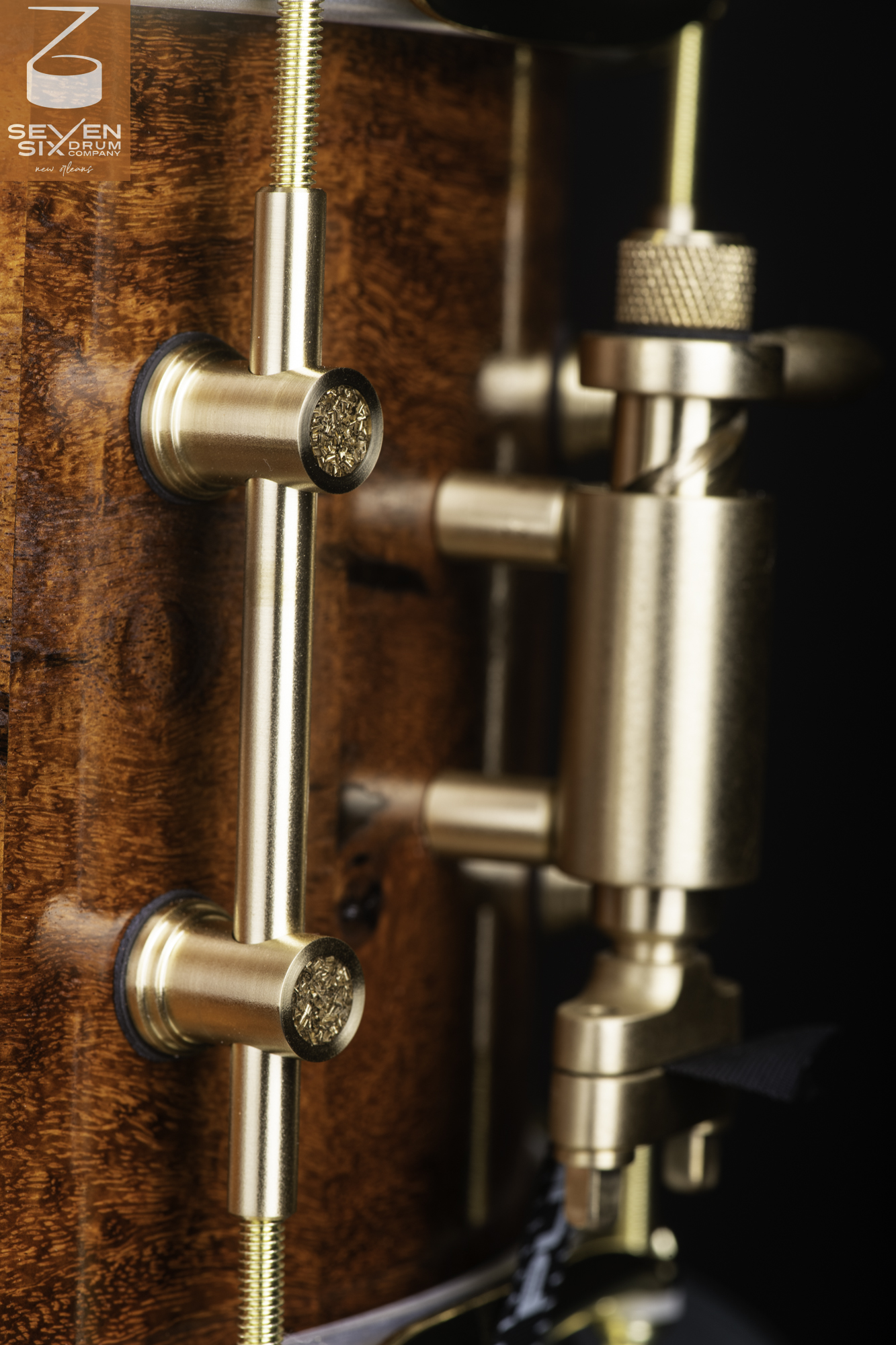 Close-up of a glossy burl wood snare drum shell with brushed brass tube lugs and a matching brass snare throw-off.