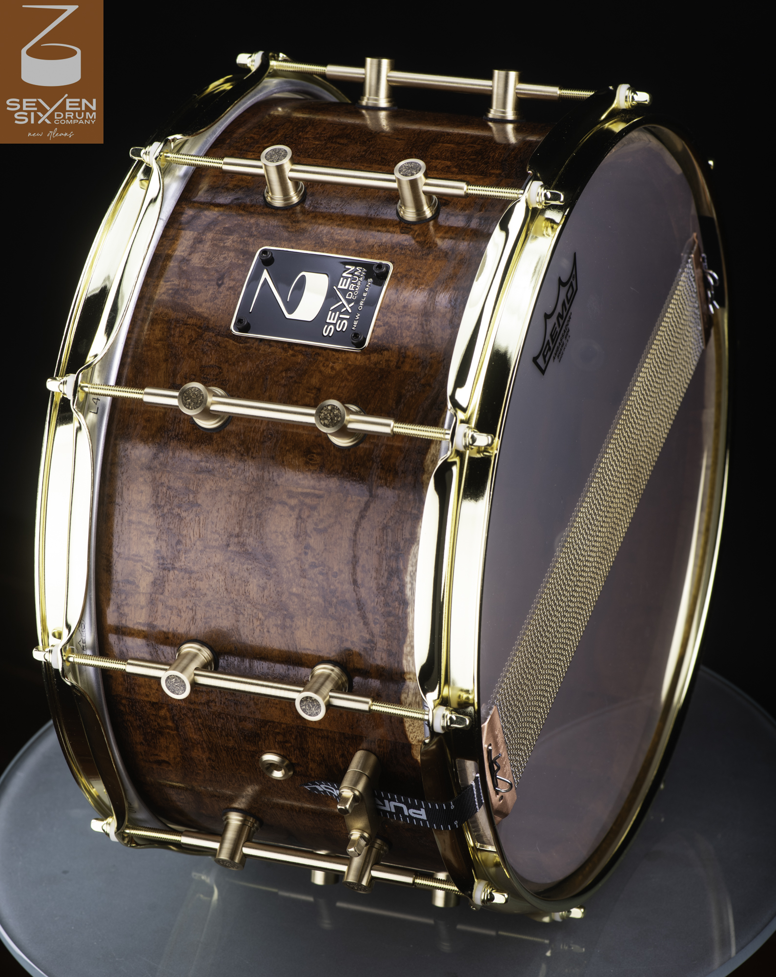 Handmade deep snare drum featuring a glossy figured wood shell with polished brass tube lugs and gold-plated rims.