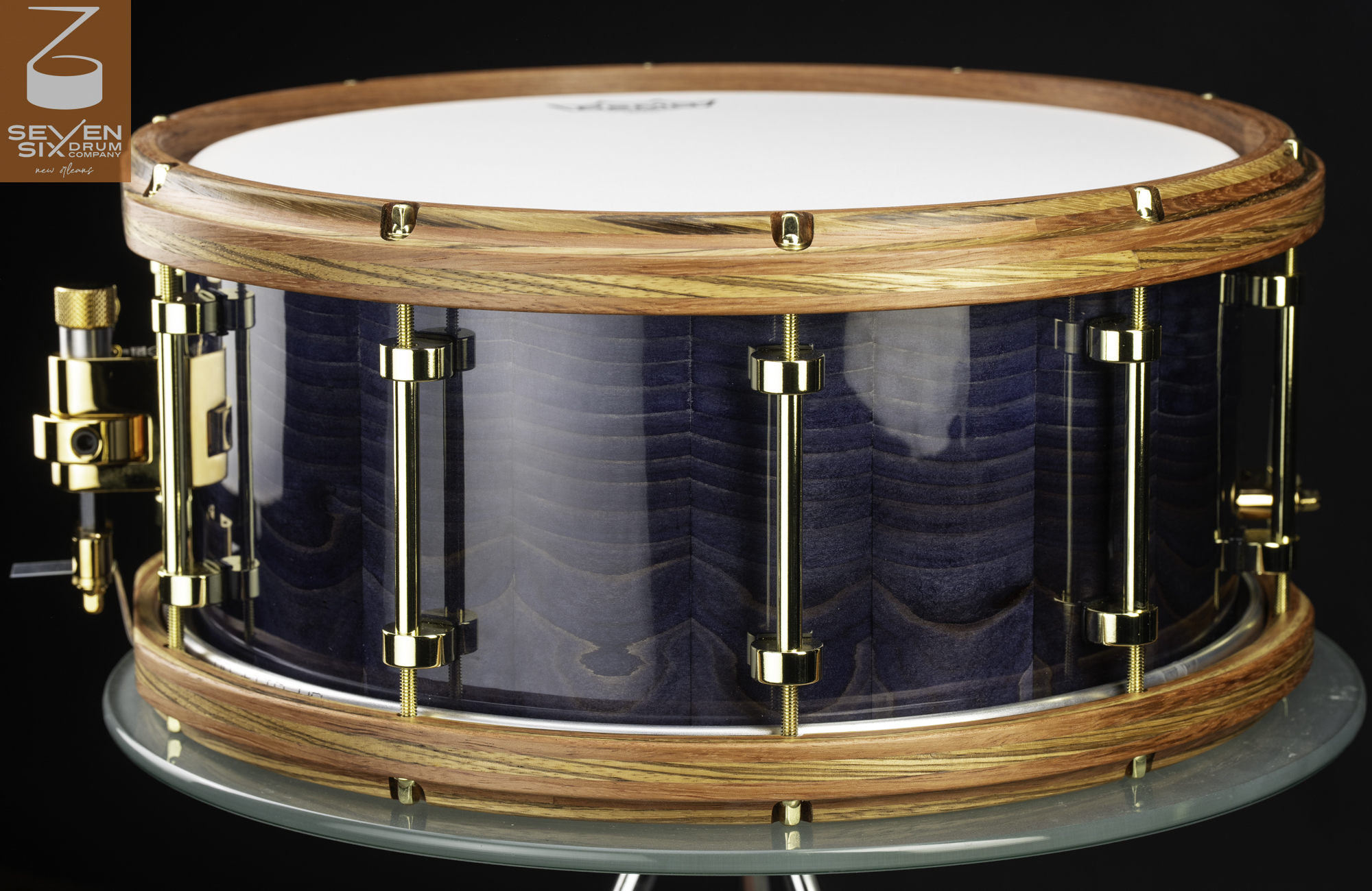 Handmade snare drum with a glossy blue wood shell, natural wood hoops, and polished brass tube lugs.