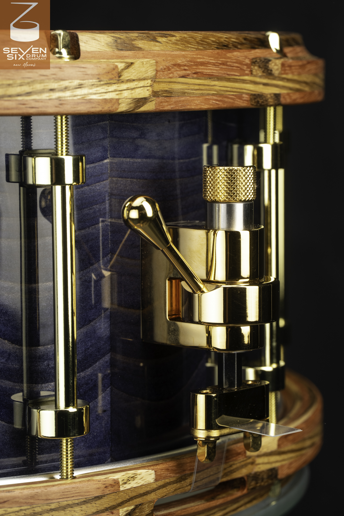 Handmade snare drum featuring a blue stained wood shell, striped wooden hoops, and a polished gold snare throw-off mechanism.