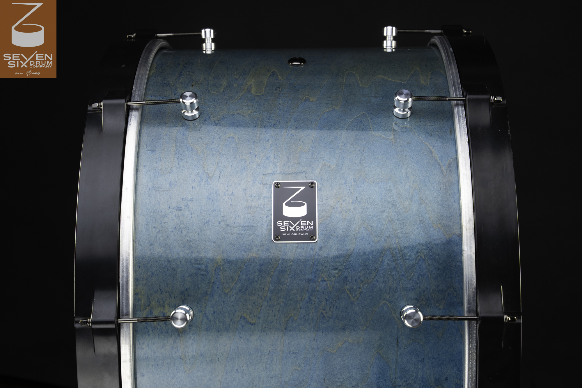 Teal-stained wood drum shell featuring wide black hoops, chrome lugs, and threaded tension rods.