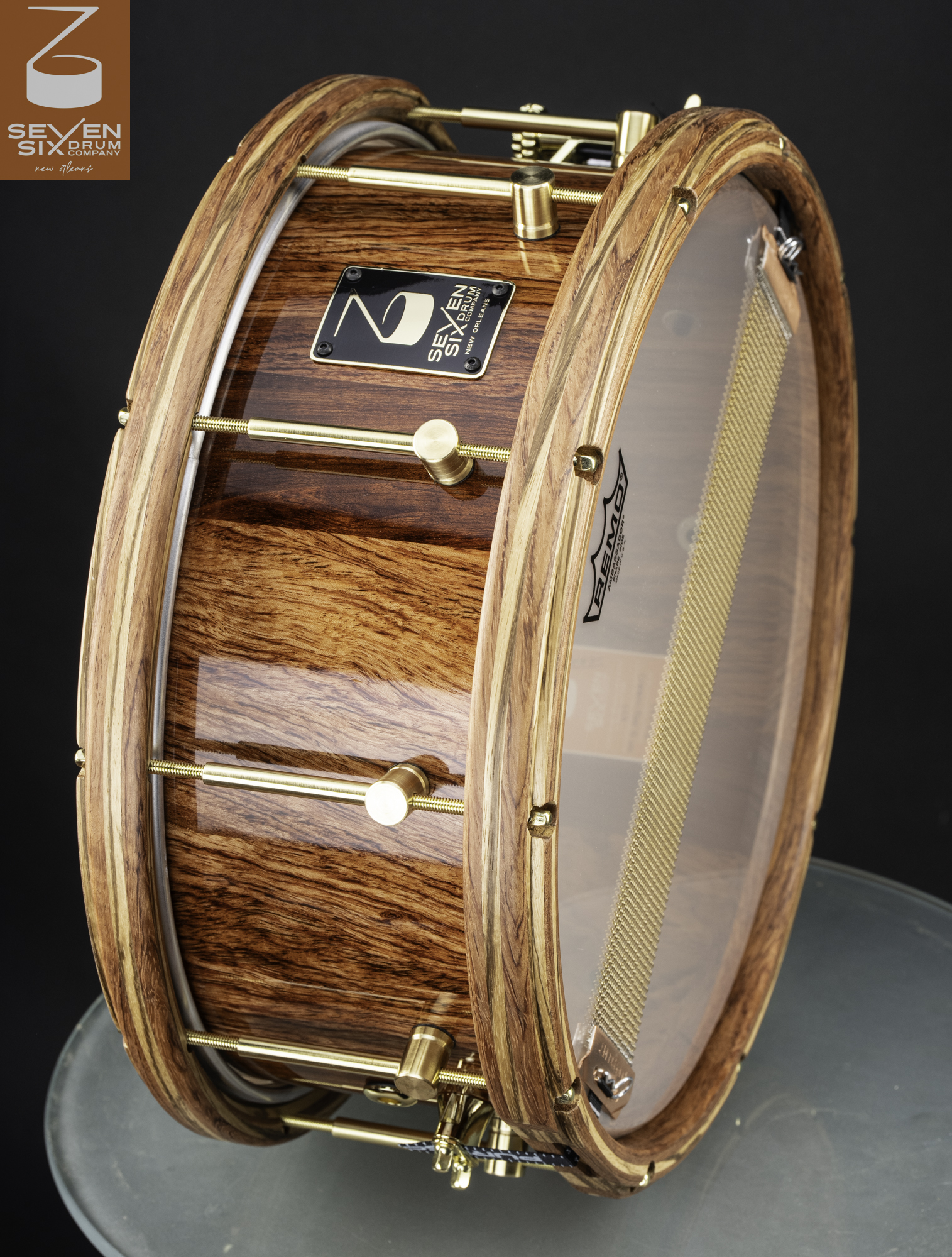 A handmade snare drum with a glossy wood shell, matching wooden hoops, and polished brass hardware.