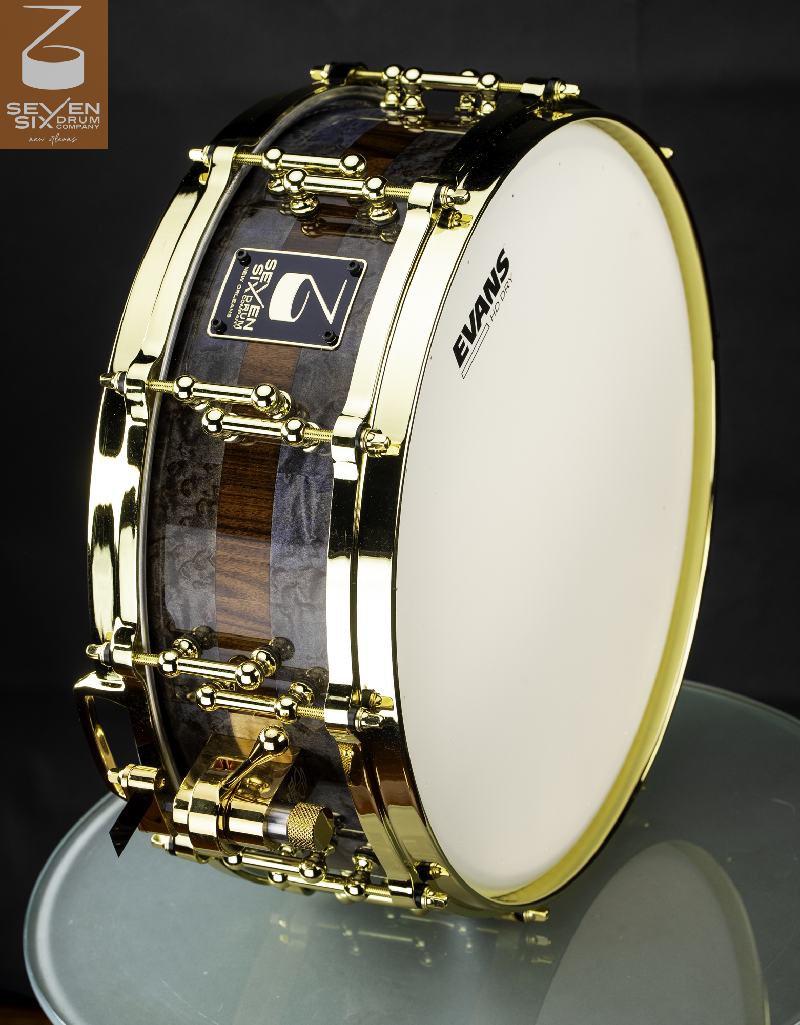 Handmade snare drum with a high-gloss grey burl and natural wood shell, outfitted with polished gold hardware and hoops.