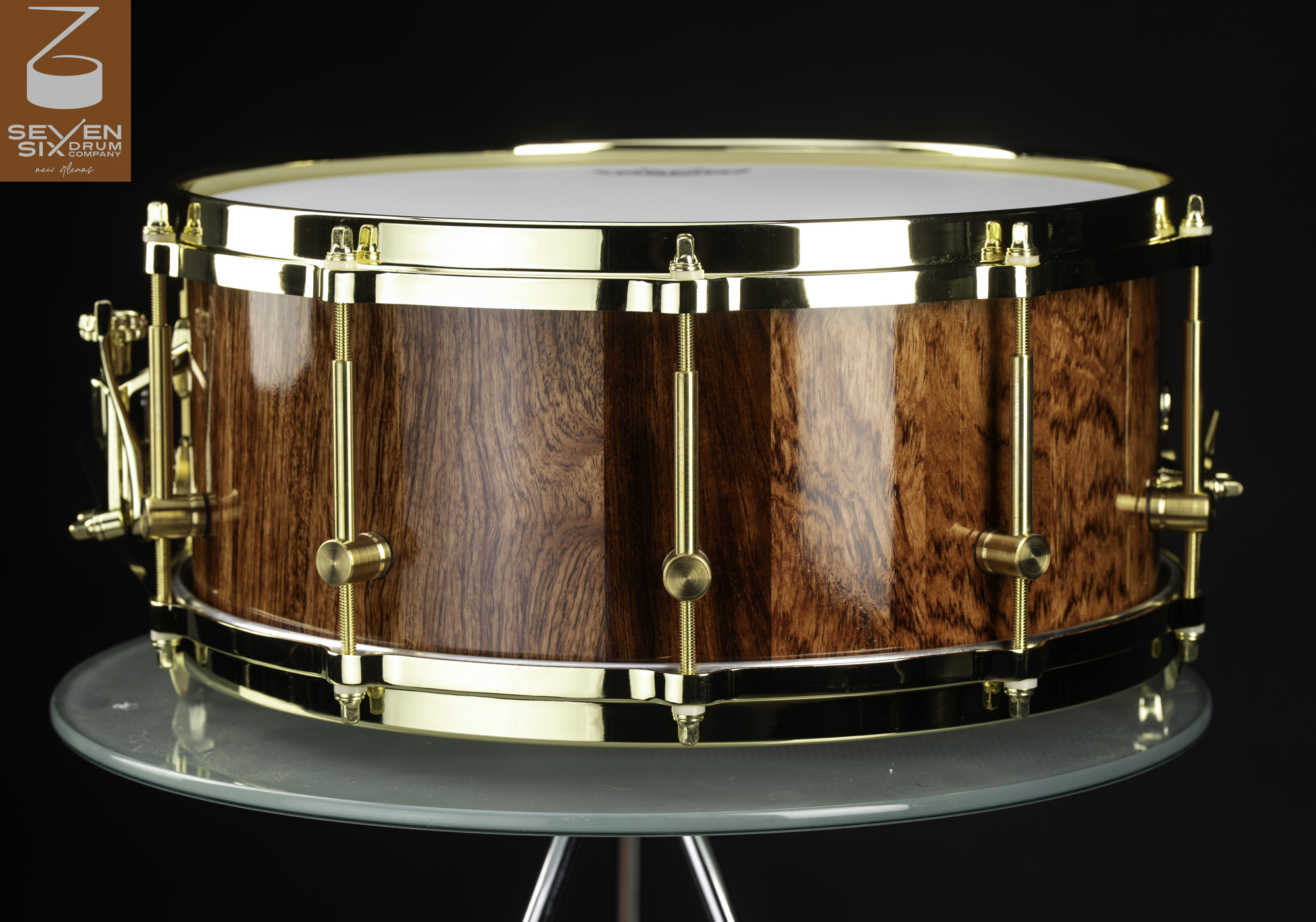 Handmade snare drum with a glossy natural wood shell, polished brass hoops, and brass lugs.