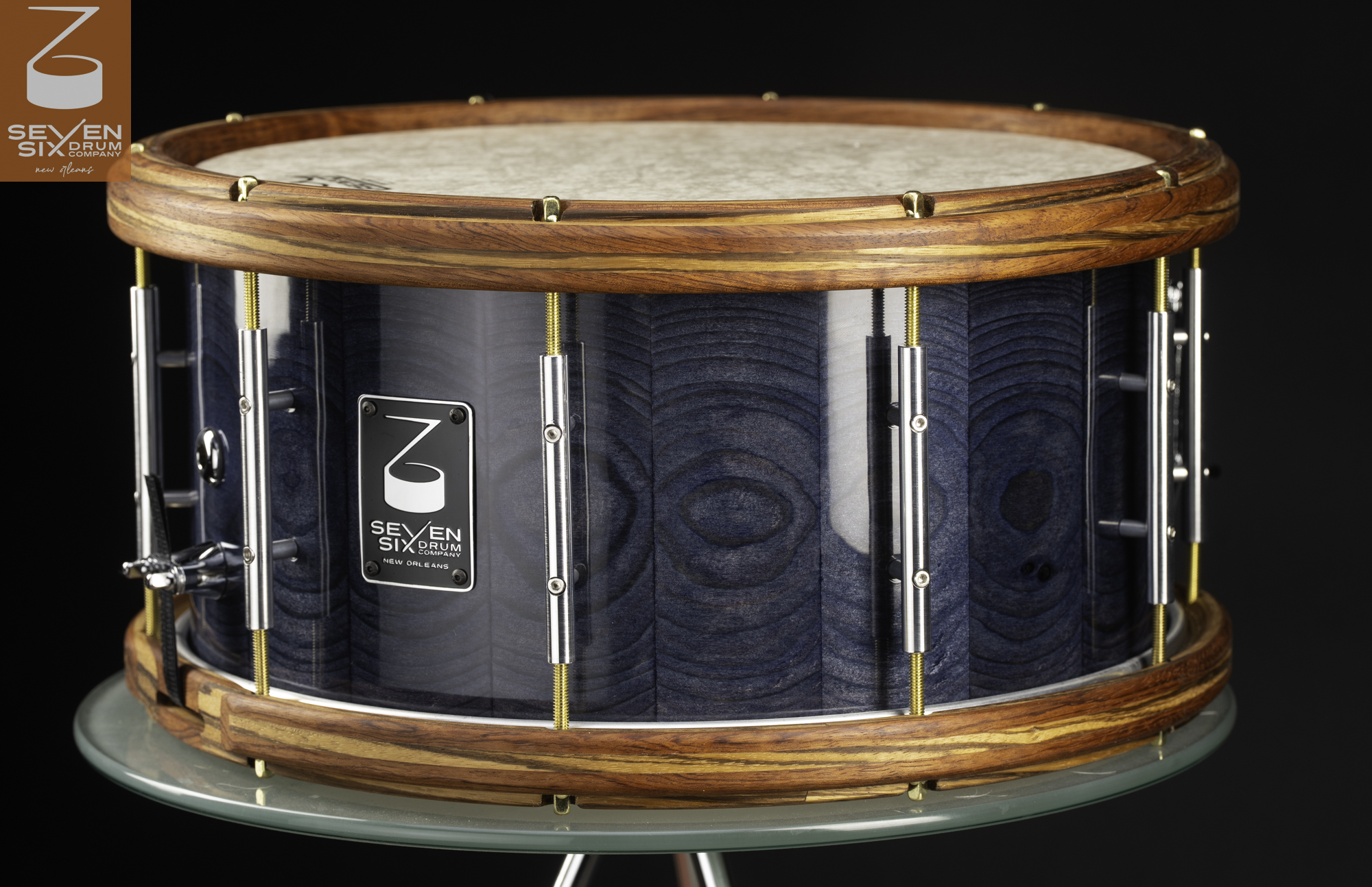 Handmade snare drum featuring a gloss blue wood shell, striped wooden hoops, and chrome tube lugs with brass tension rods.