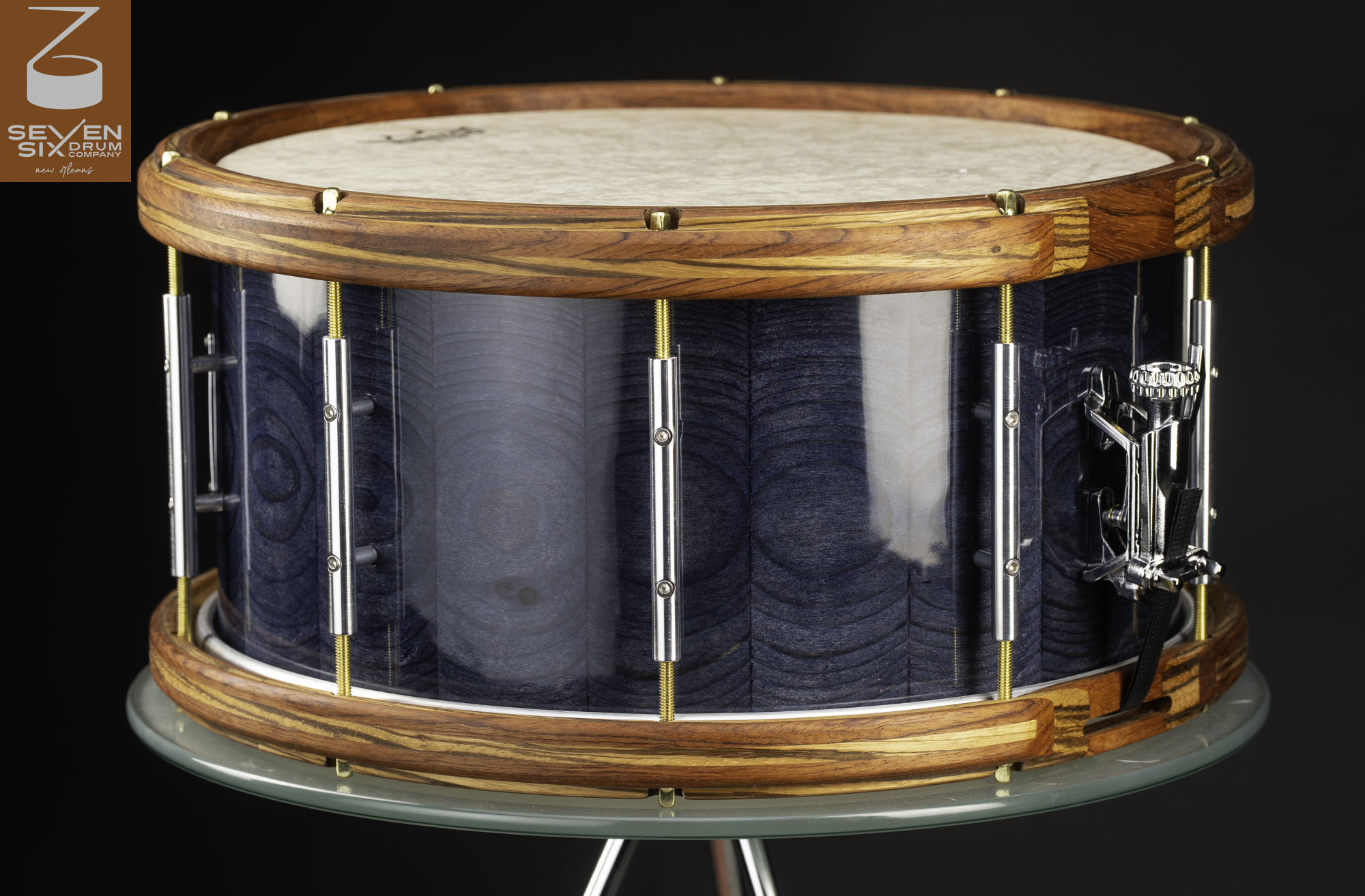 Handmade snare drum with a glossy blue wood shell, natural wood hoops, chrome tube lugs, and brass tension rods.