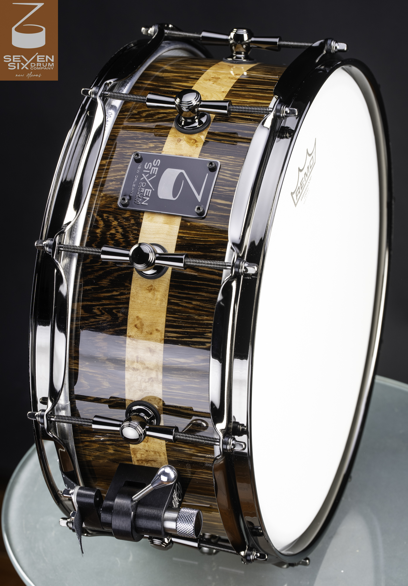 Handmade snare drum with a glossy dark exotic wood shell, light center stripe, and polished black nickel hardware.