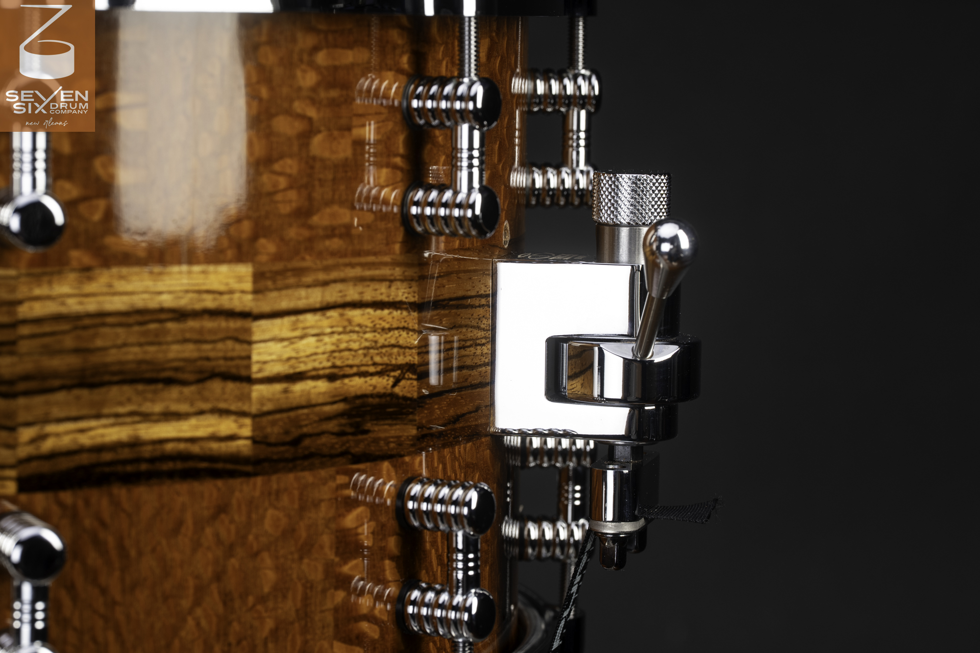 A glossy segmented wood snare drum featuring polished chrome lugs and a snare throw-off.