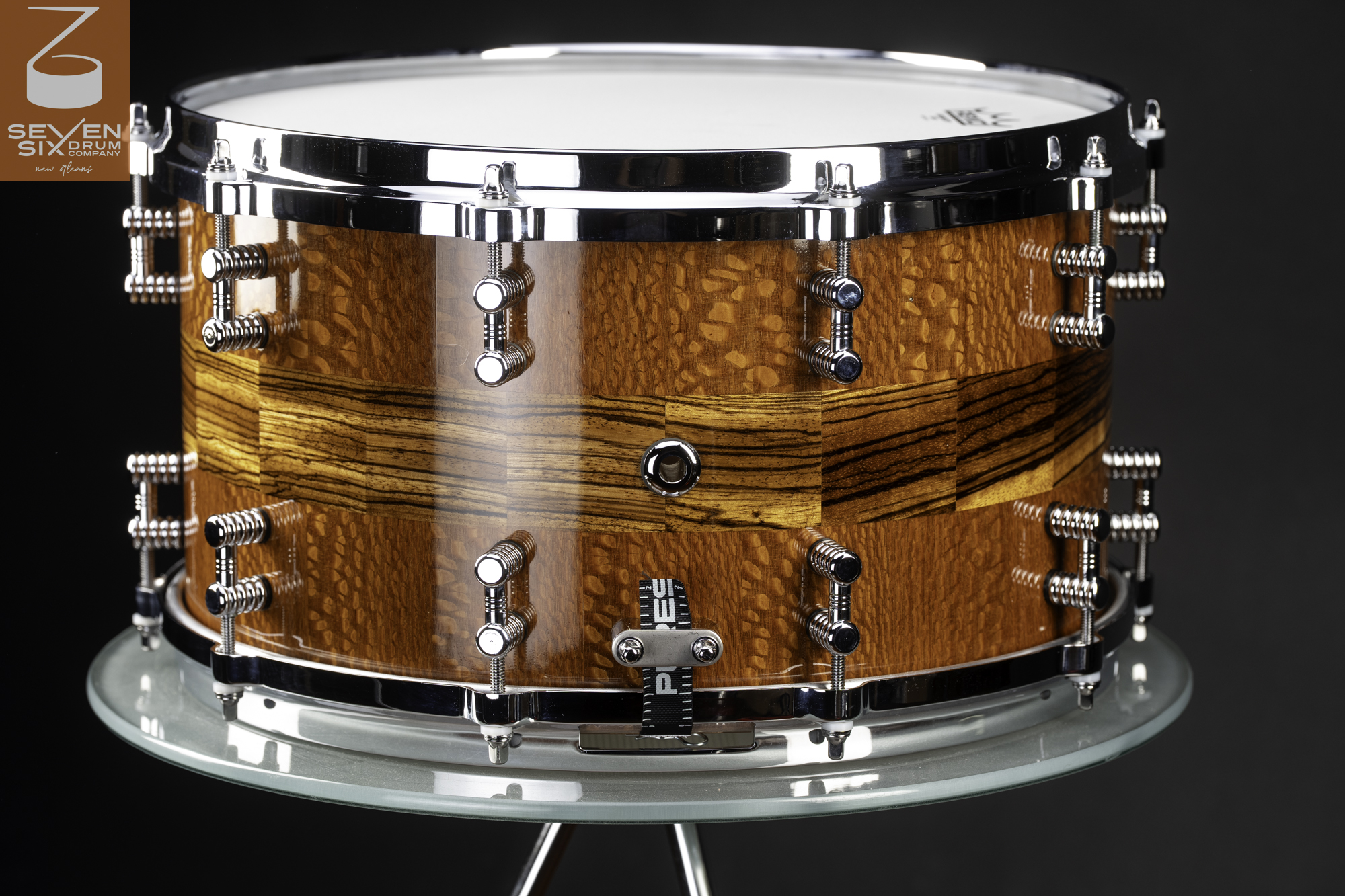 Glossy wood snare drum with lacewood and a zebrawood stripe, fitted with chrome hoops and lugs.