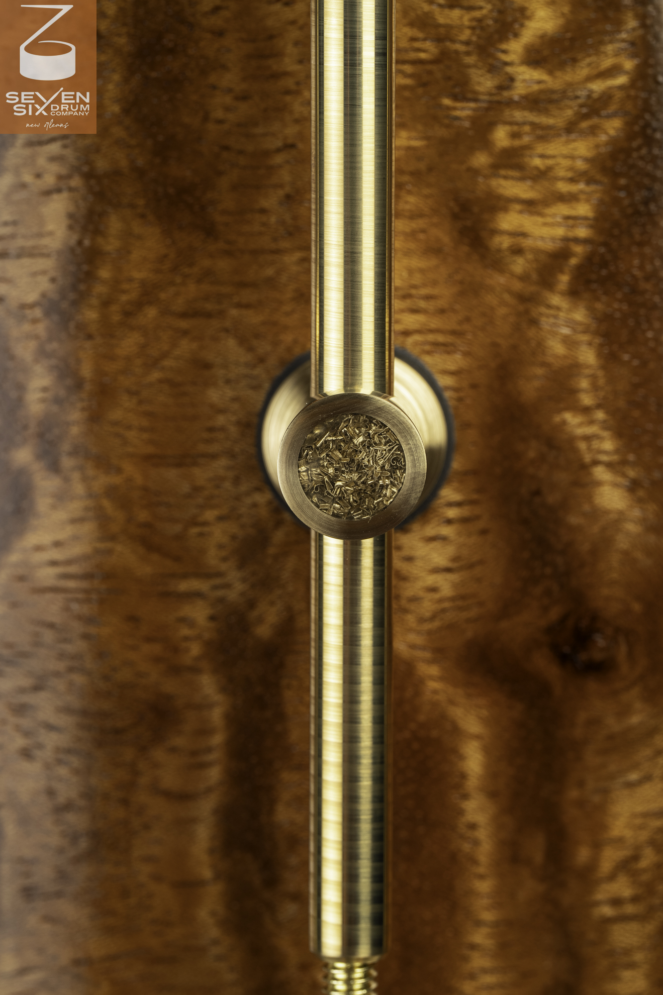 Brushed brass tube lug with brass shaving inlay mounted on a glossy, figured wood snare drum shell.