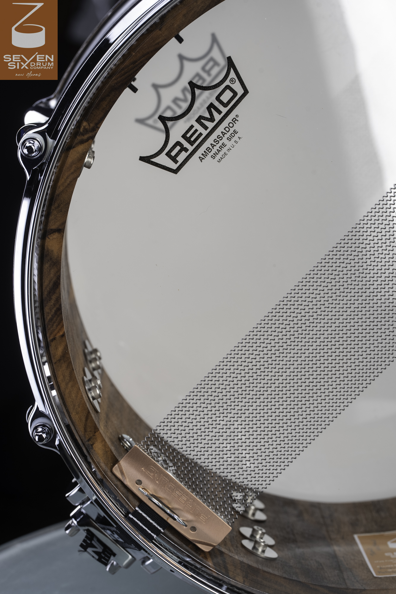 Bottom view of a natural-finish wood snare drum with a clear Remo head, chrome hoop, and PureSound snare wires.