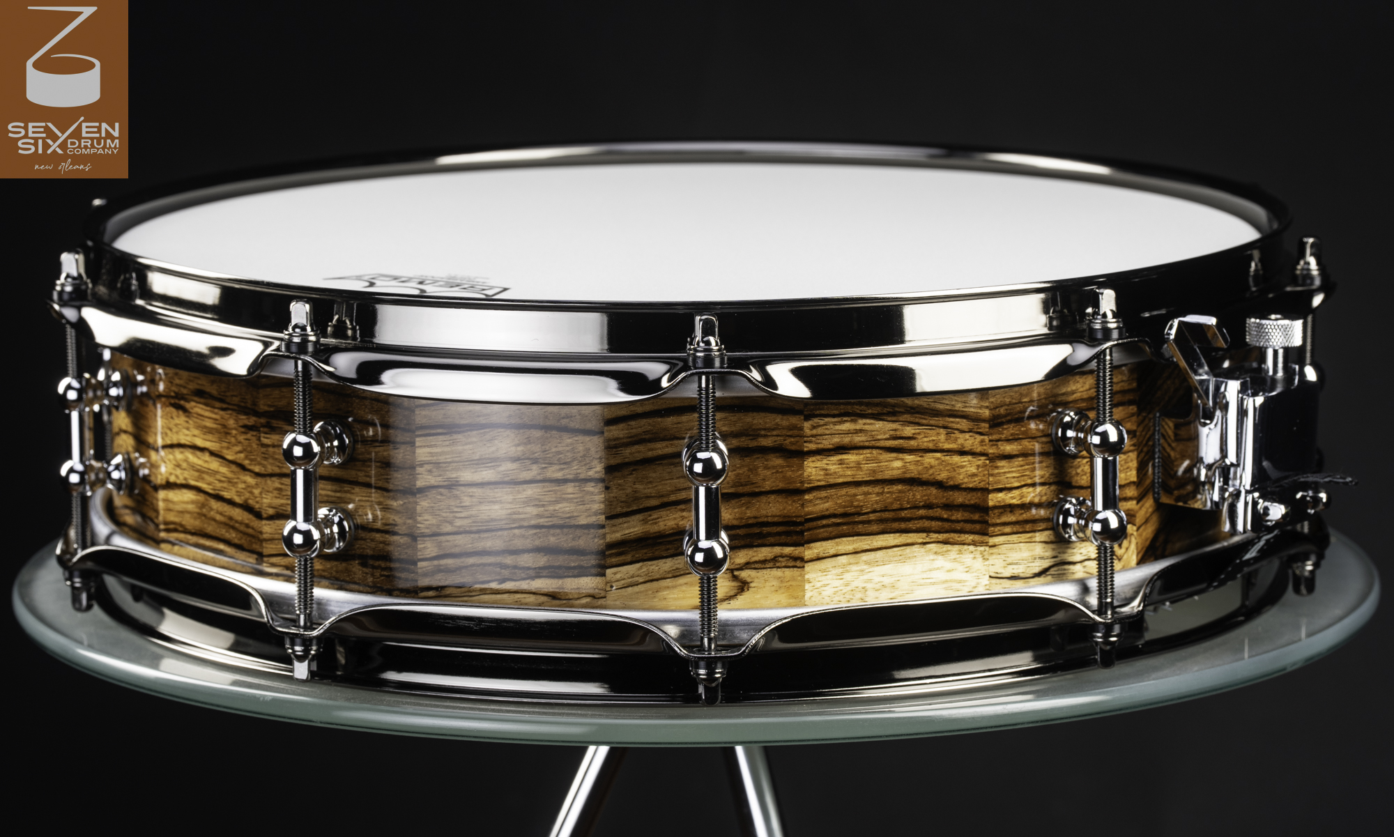 Handmade snare drum featuring a glossy zebrawood shell with polished chrome tube lugs and hoops.