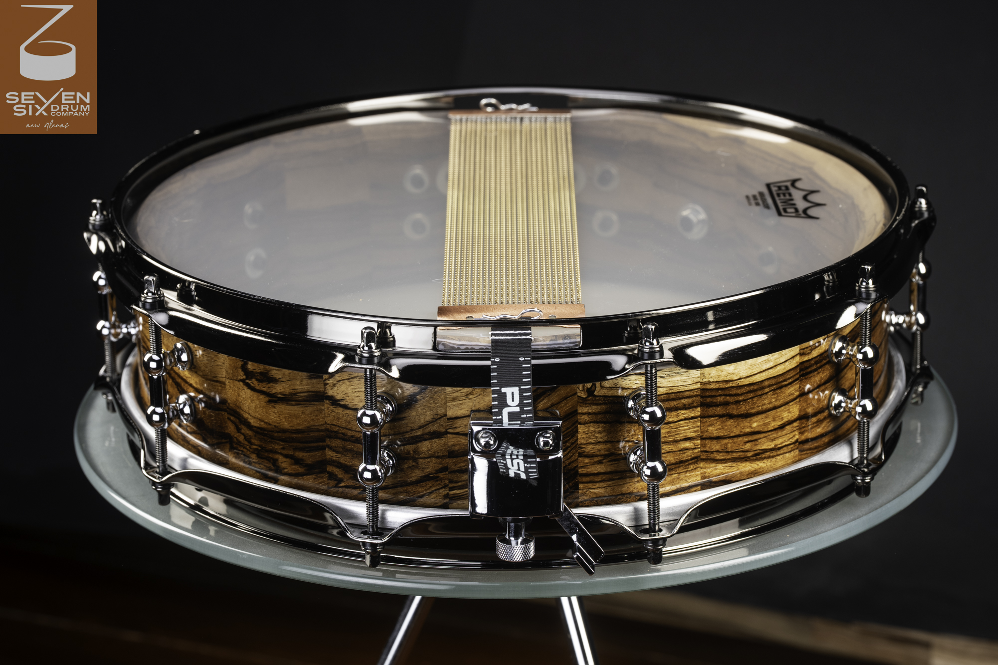 Handmade snare drum with a glossy zebrawood shell, black nickel hardware, tube lugs, and brass snare wires.