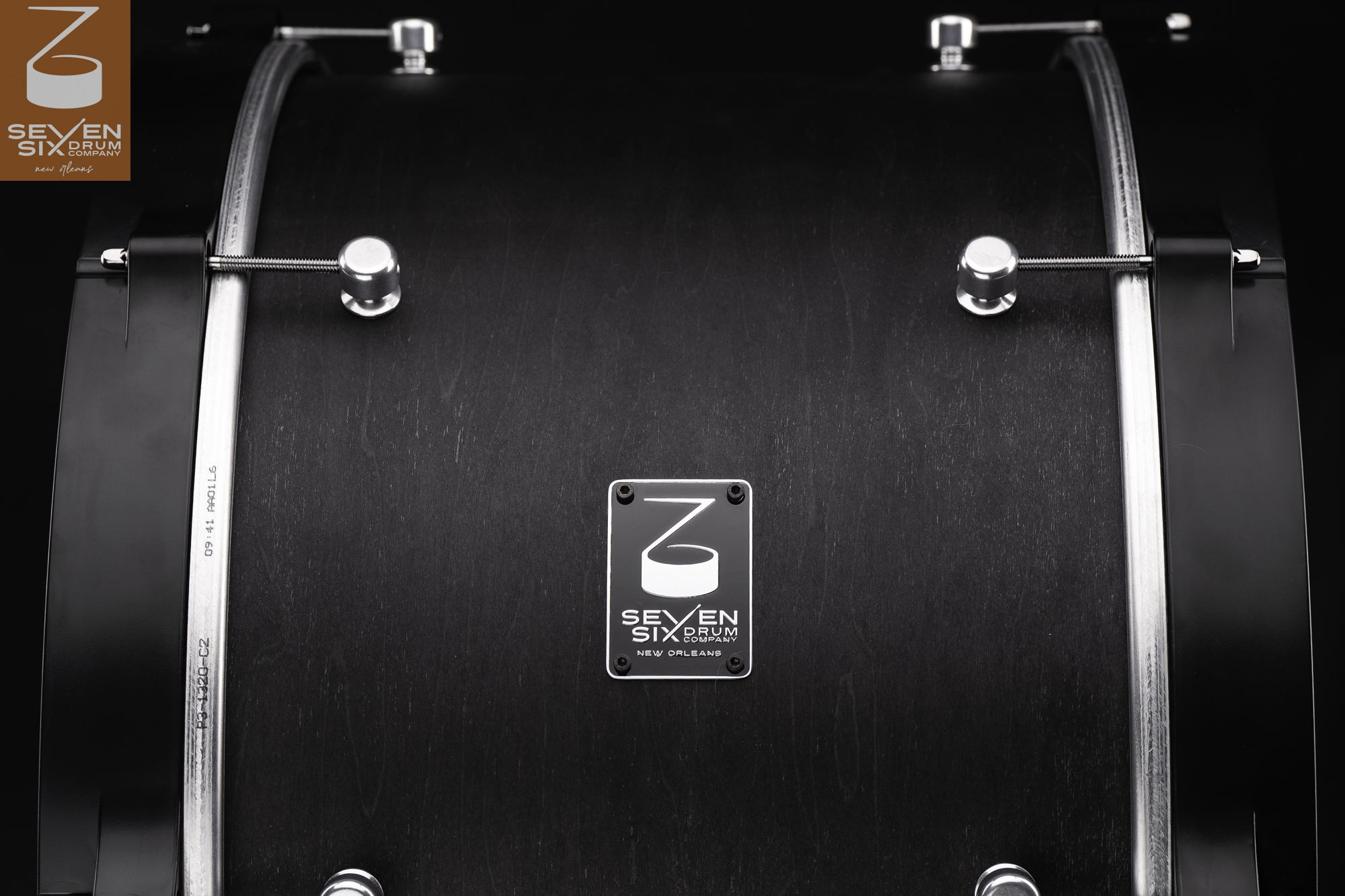 Matte black wood drum shell featuring black hoops, round chrome lugs, and a Seven Six Drum Company badge.
