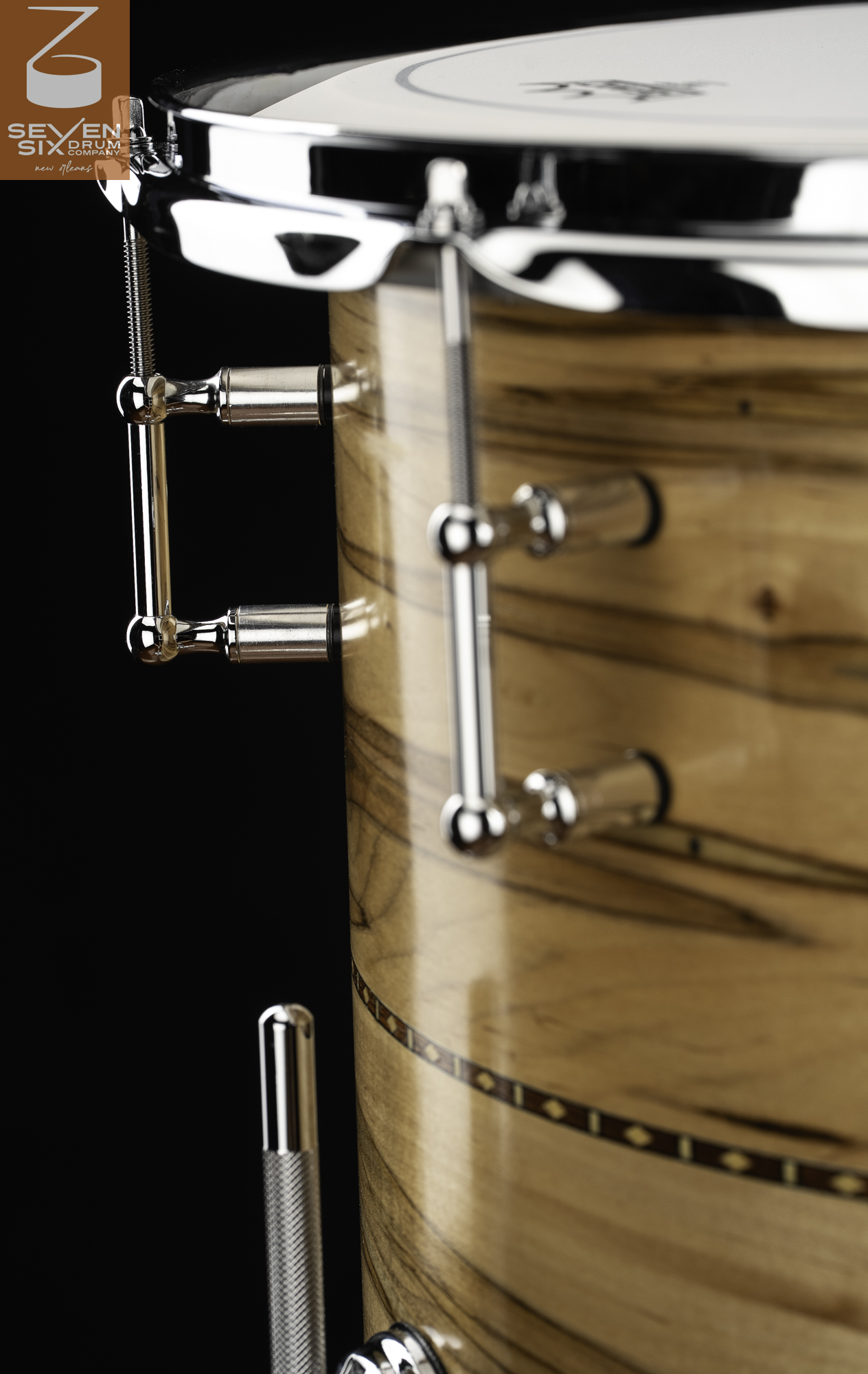 Glossy natural wood snare drum featuring a decorative inlay band, chrome tube lugs, and a polished rim.
