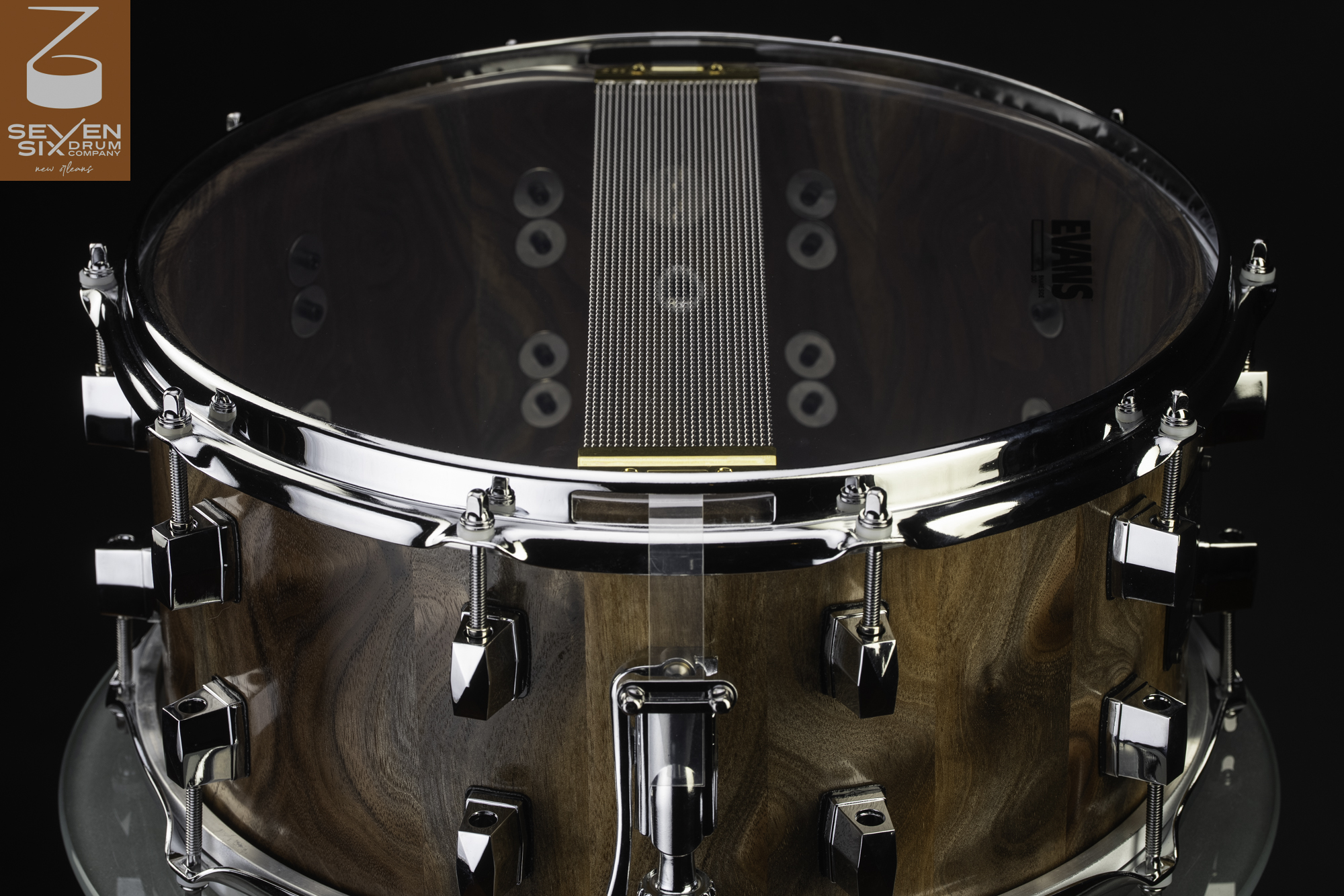 Handmade walnut snare drum with a natural finish, chrome hardware, and snare wires across a clear resonant head.