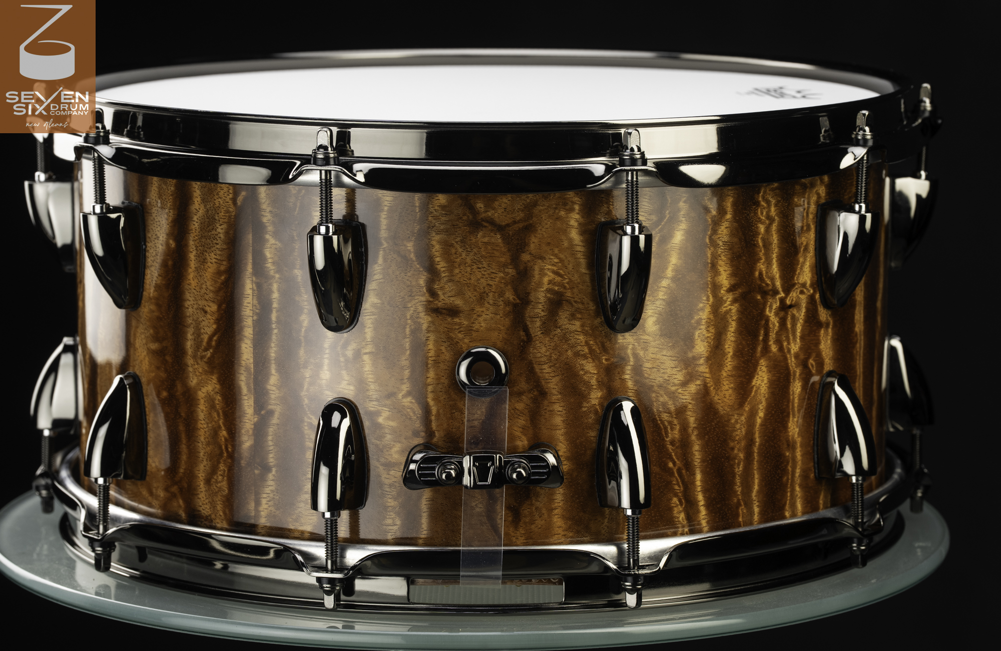 Handmade snare drum featuring a glossy figured wood shell with polished black nickel lugs and hoops.