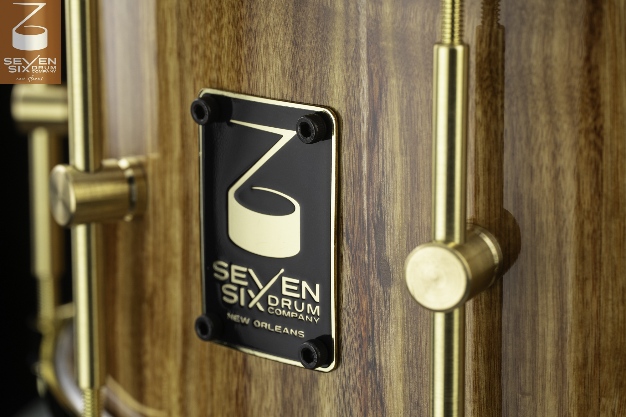 Glossy wood snare drum featuring a black Seven Six logo badge and brushed brass tube lugs.