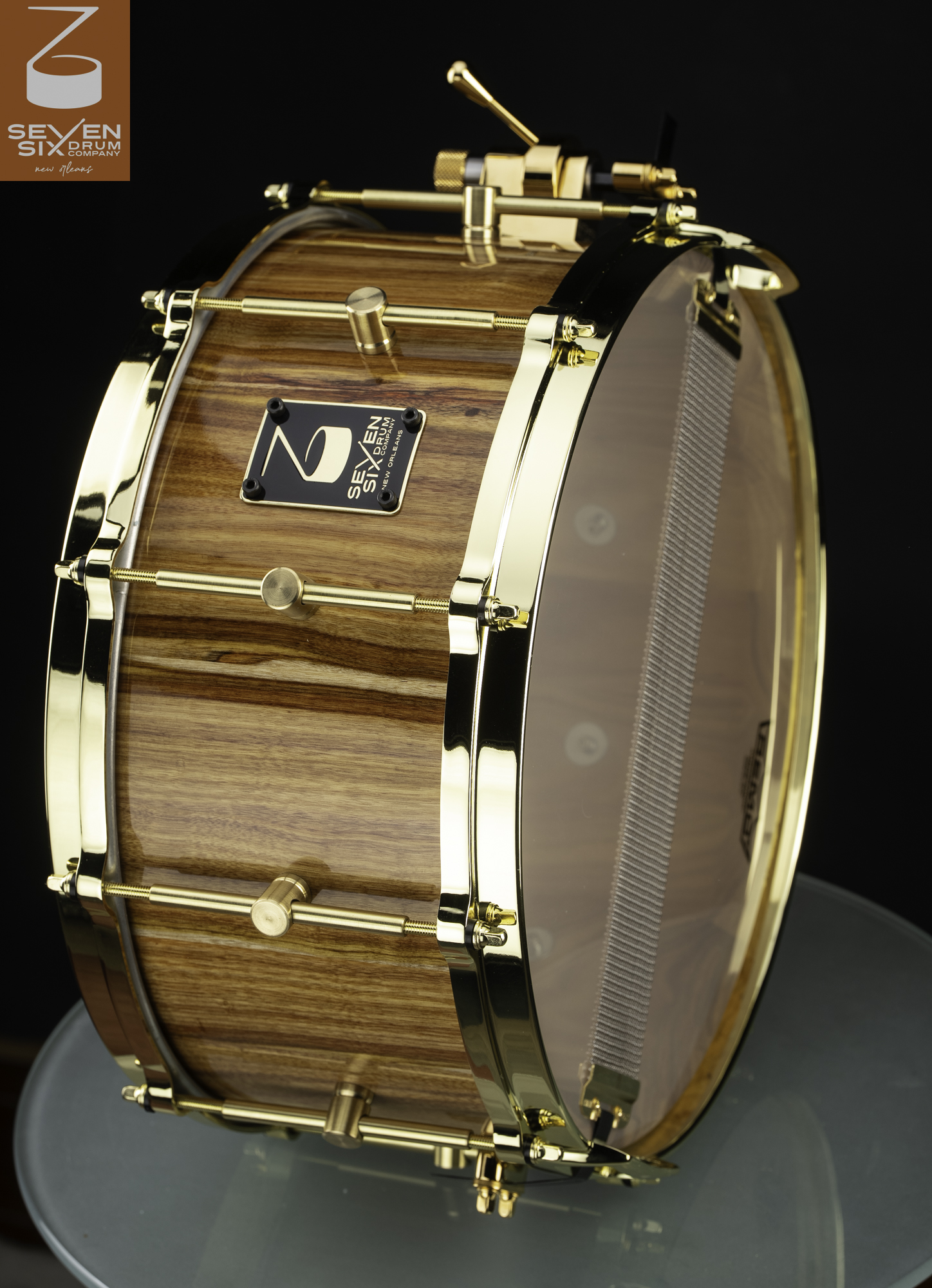 Glossy striped wood snare drum fitted with polished gold hoops, single-point lugs, and a snare throw-off.
