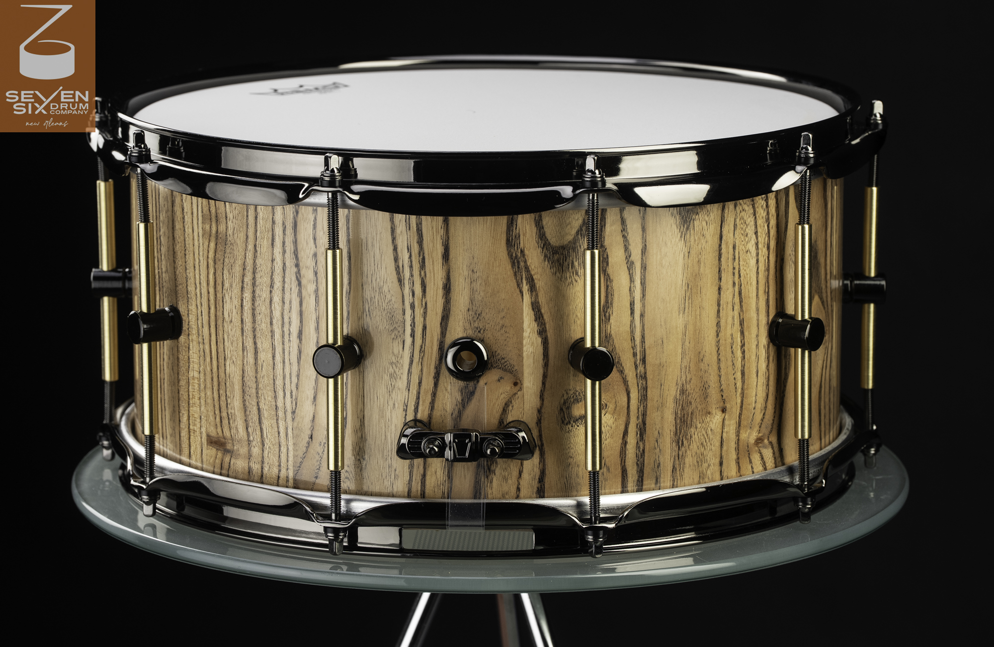 Handmade snare drum with a natural-finish wood shell, black nickel hoops, and brass and black tube lugs.