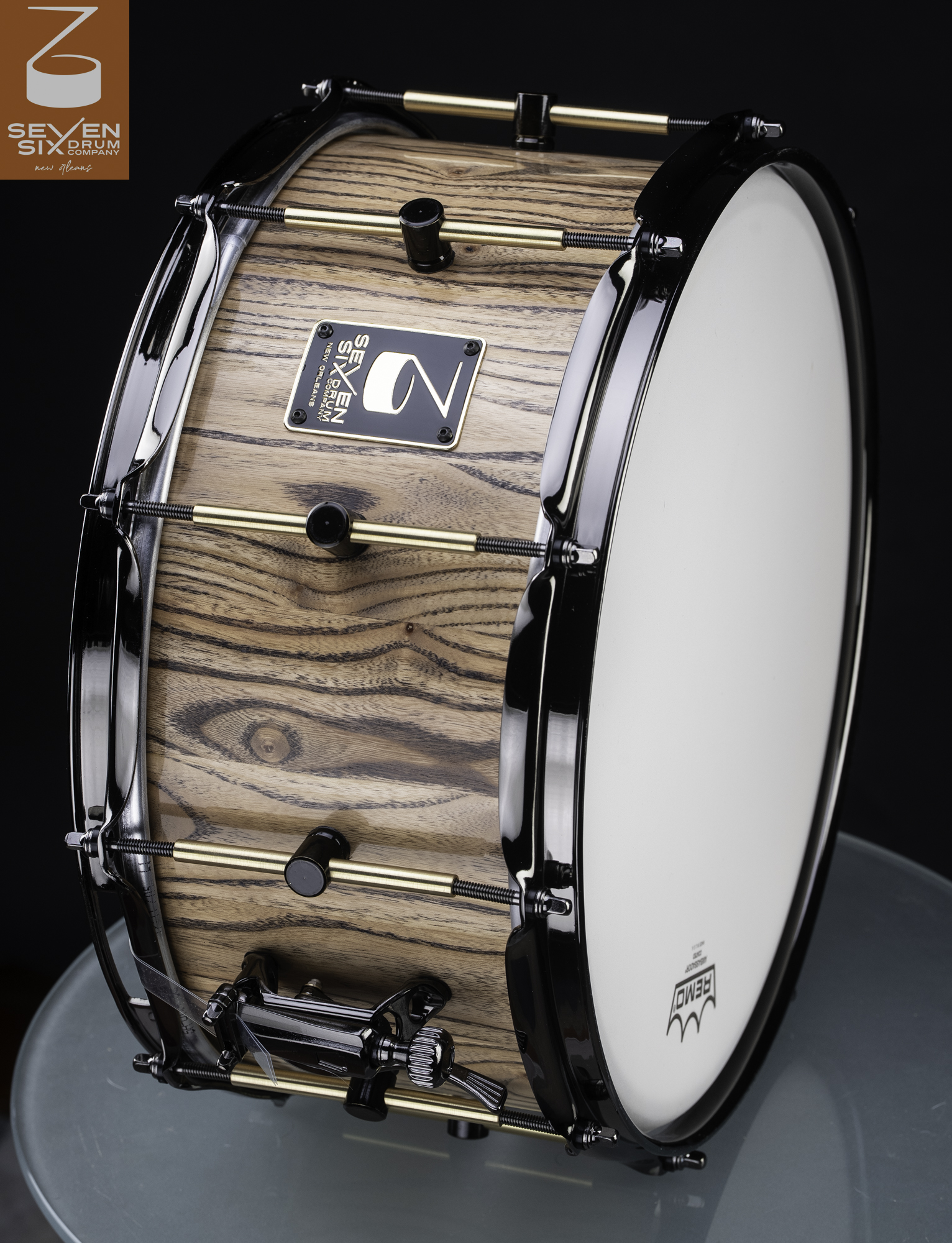 Natural wood snare drum with bold horizontal grain, clear finish, black hoops, and brass tube lugs.