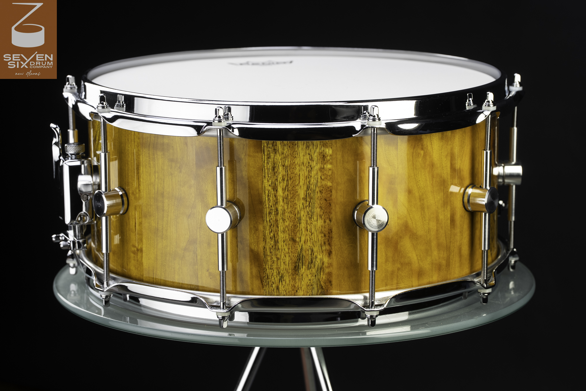 Handmade snare drum with a glossy amber wood shell, chrome hoops, and single-point round lugs.
