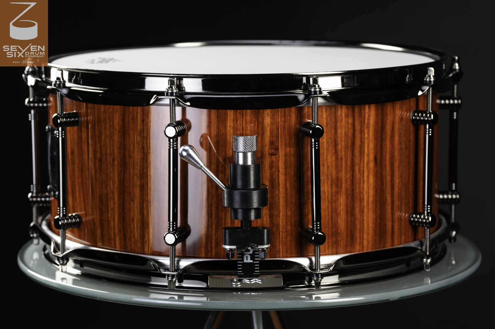 Handmade snare drum with a gloss reddish-brown wood shell, black nickel hardware, tube lugs, and a Trick throw-off.