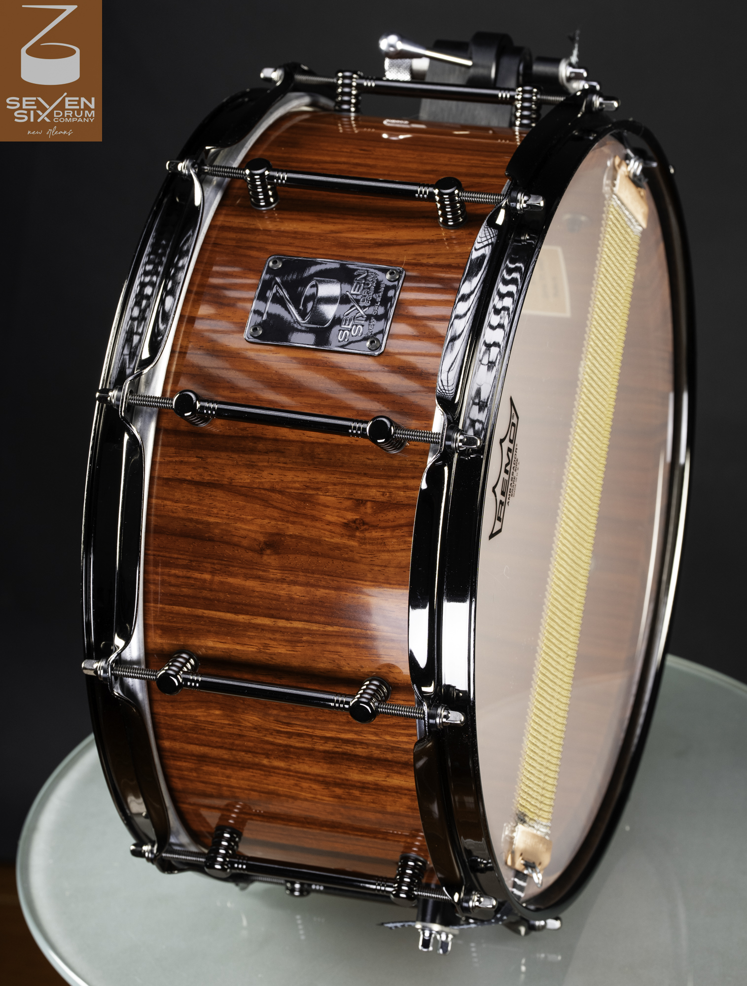A deep snare drum with a glossy reddish-brown wood shell, black nickel hoops, and matching tube lugs.