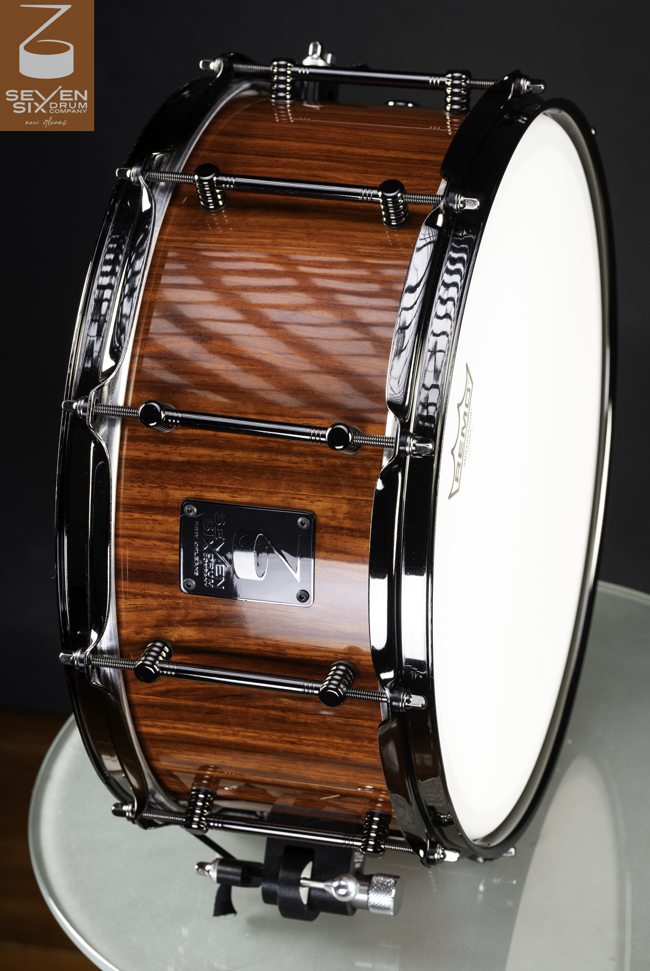 Handmade snare drum with a glossy reddish-brown wood shell, polished black chrome hoops, and tube lugs.