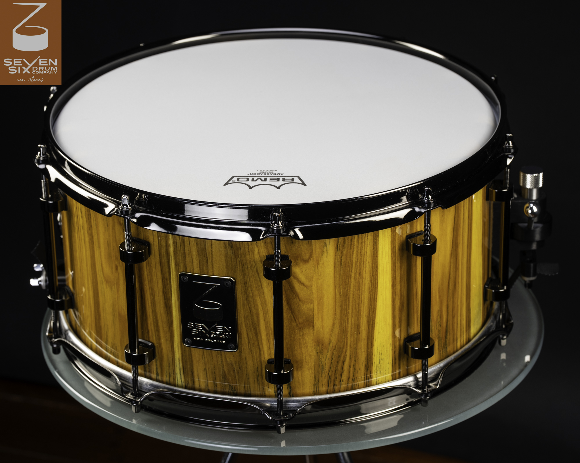 Snare drum featuring a glossy vertical-grain wood shell with black nickel hoops and lugs.