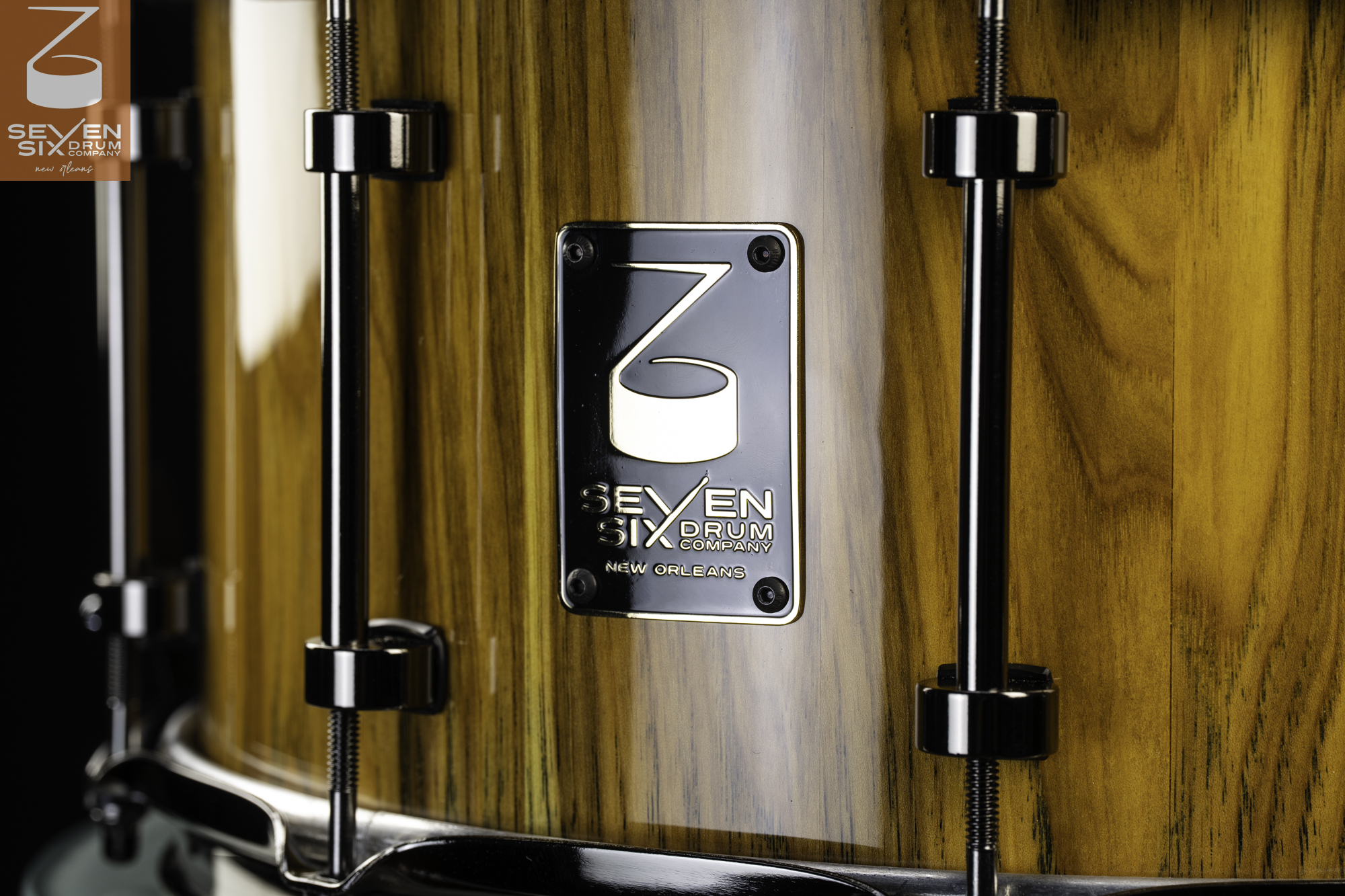 Snare drum shell in a high-gloss wood grain finish with black nickel tube lugs and a metal logo badge.