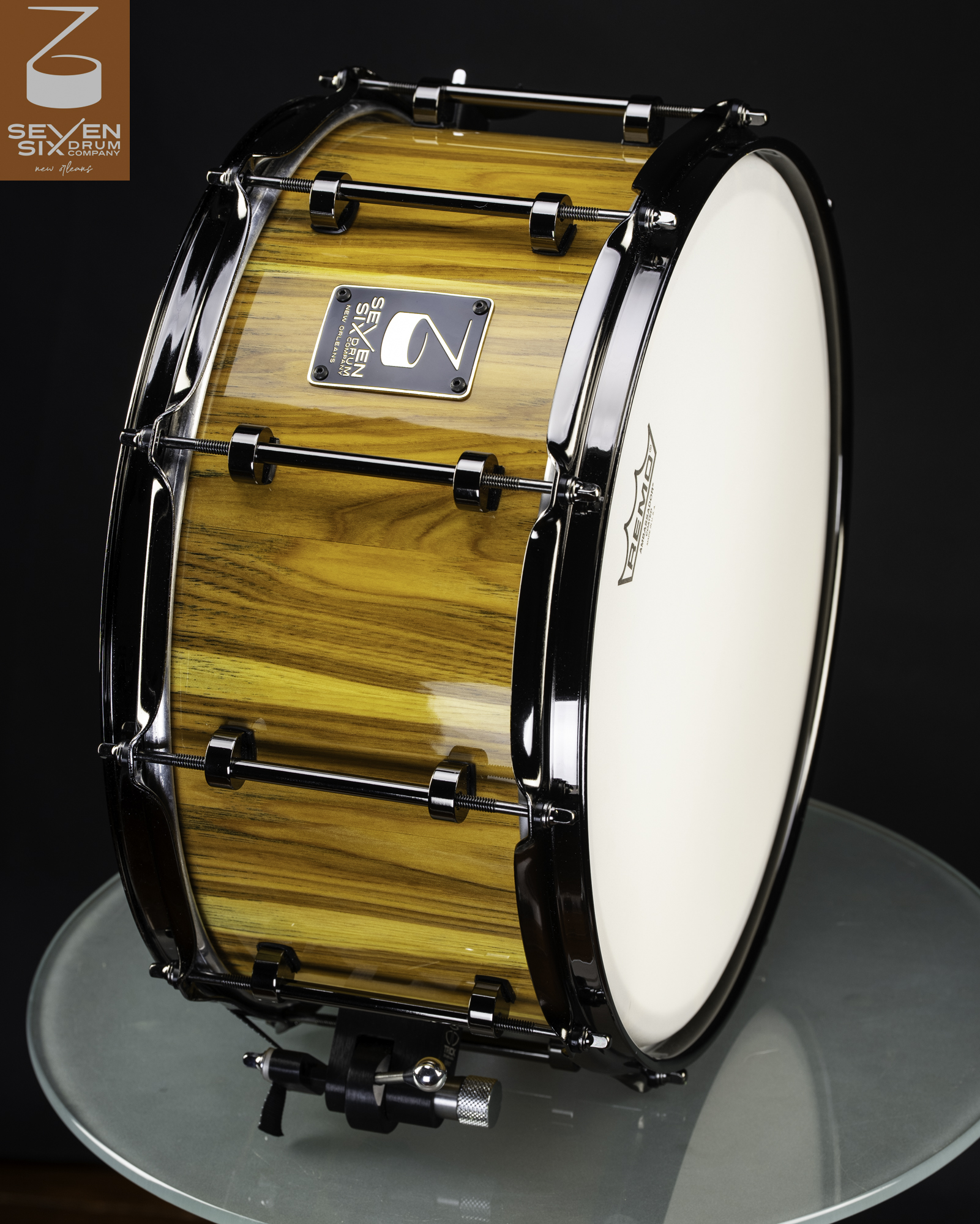 Handmade snare drum featuring a glossy amber wood shell with black nickel tube lugs and hoops.