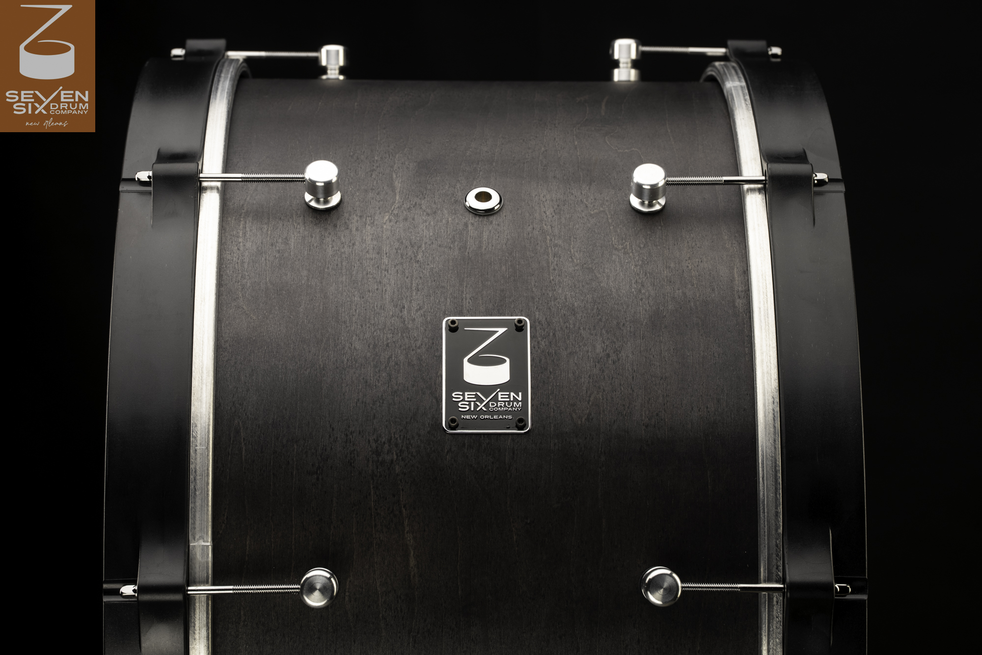 Dark matte-finish wood drum shell with black wooden hoops, round silver lugs, and claw-hook tension rods.