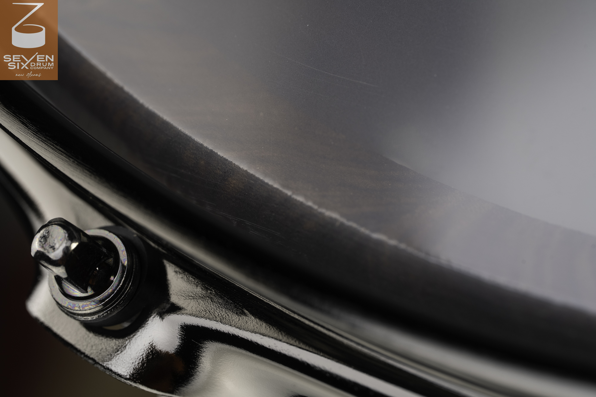 Close-up of a dark wood snare drum featuring a glossy black metal hoop, matching tension rod, and smooth black drumhead.
