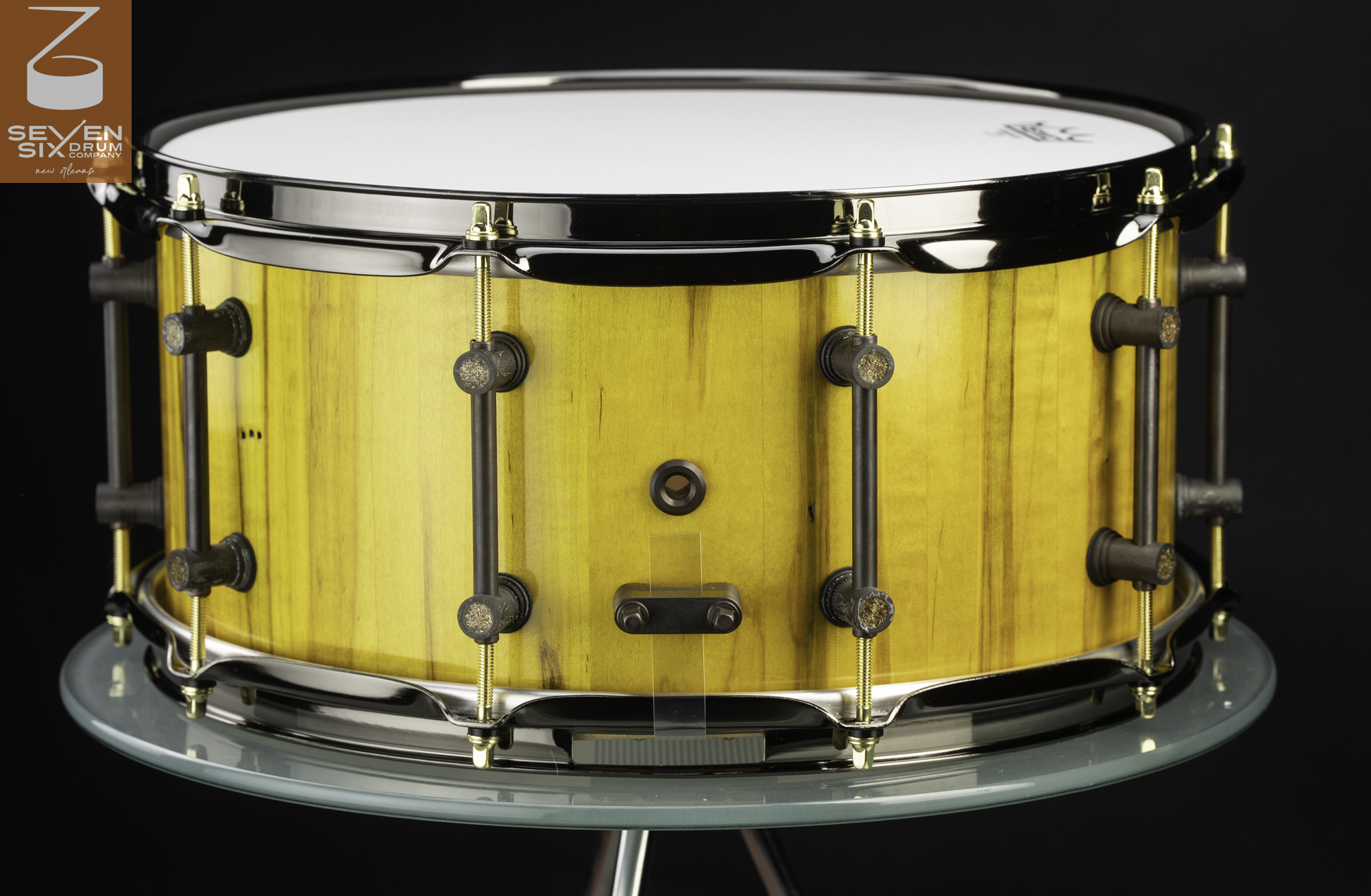Handmade snare drum featuring a glossy yellow wood shell, dark tube lugs, gold tension rods, and black nickel hoops.