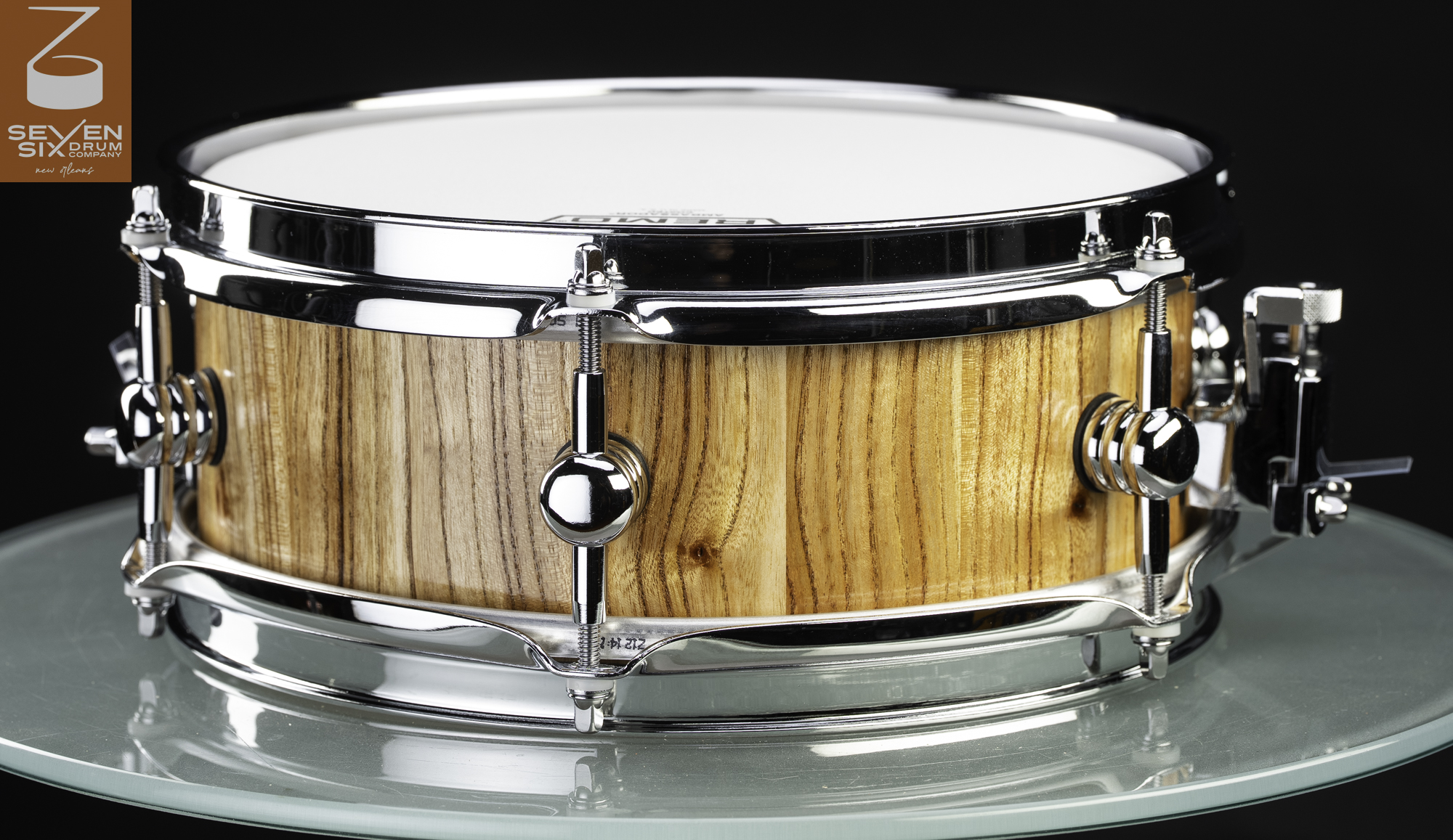 Handmade snare drum featuring a natural wood stave shell with a clear finish, chrome hoops, and rounded center lugs.