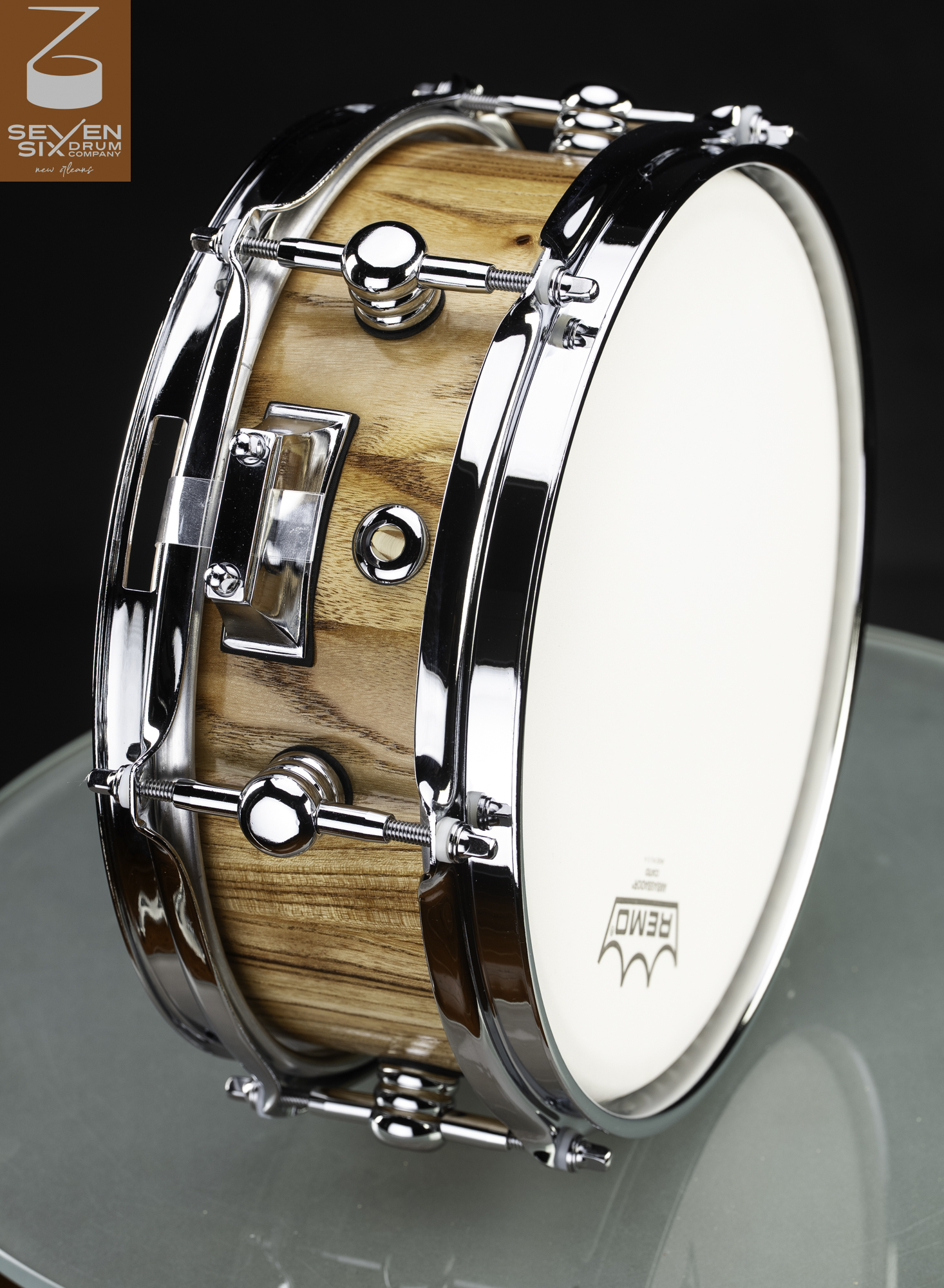 Handmade snare drum featuring a clear-finish natural wood shell, polished chrome hoops, round lugs, and a white Remo drumhead.